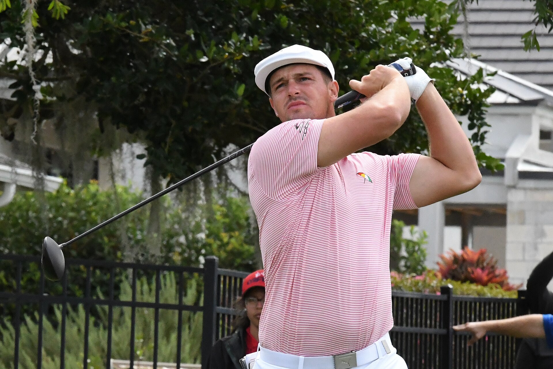 Bryson DeChambeau mid-swing wearing a pink polo shirt at a golf tournament