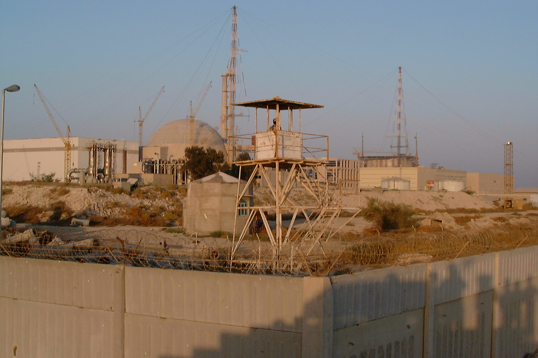 Bushehr Nuclear Power Plant on Iran's Gulf coast, showing reactor containment dome, security perimeter and guard tower, with construction cranes for the second unit in the background