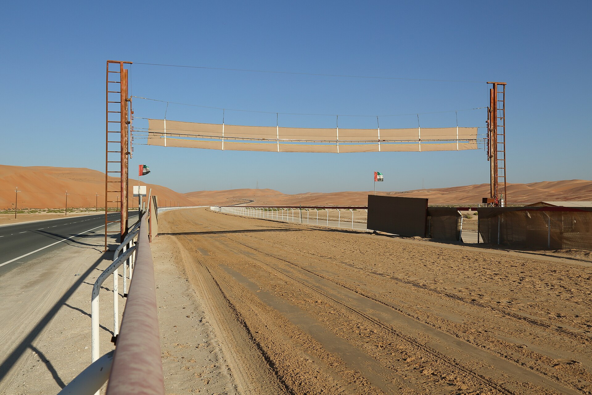 A camel race track stretching across Arabian desert landscape with railings, sand surface, and dunes in the background