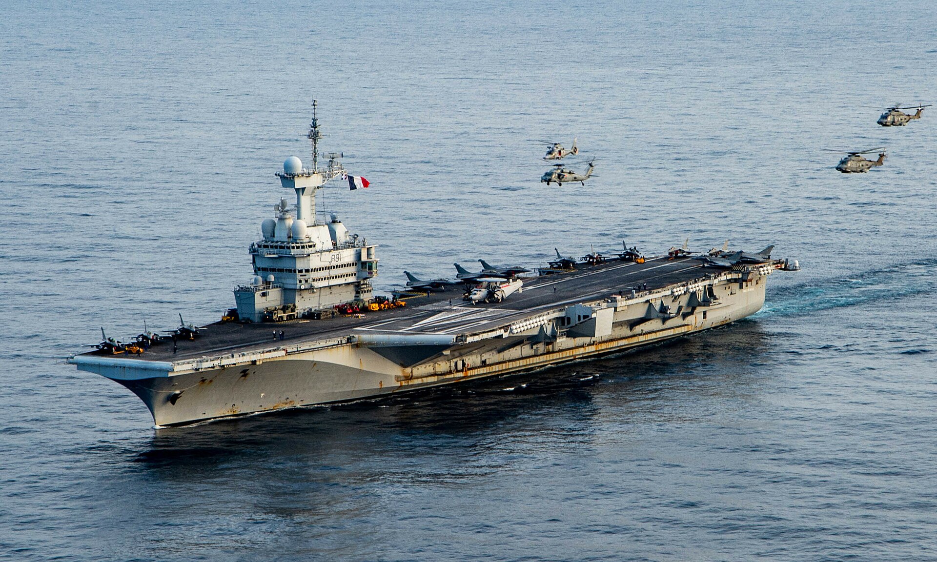French aircraft carrier Charles de Gaulle (R91) underway in the Ionian Sea on 17 March 2022, with Rafale fighters and helicopters on deck — the only non-American nuclear-powered carrier in operation, positioned for the European Hormuz coalition