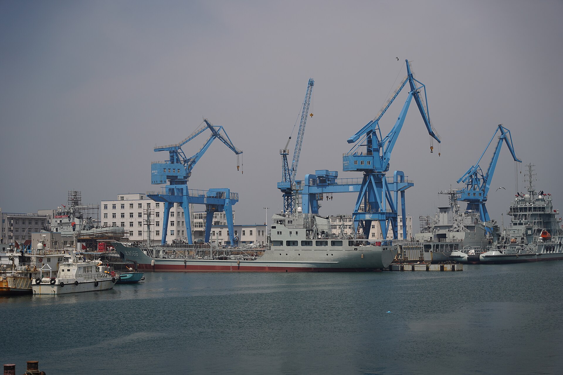 A Chinese tanker vessel docked at Qingdao port in China, with blue industrial cranes rising above the waterfront — Chinese teapot refineries handle approximately 90 percent of Iran oil exports to China