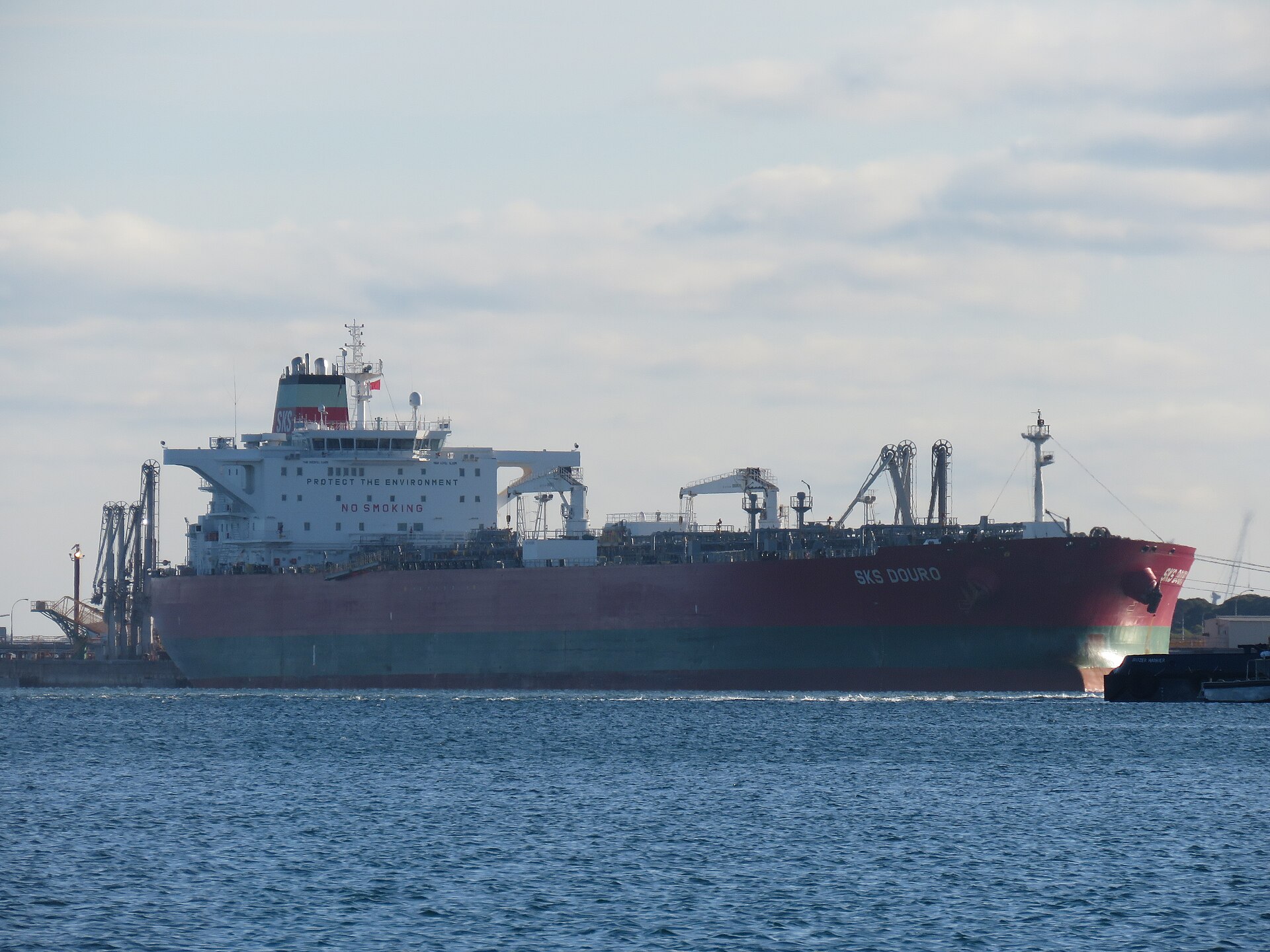 Crude oil tanker SKS Douro berthed at an oil refinery jetty for unloading, illustrating the term-contract delivery relationship between Saudi Aramco and its Asian refinery customers