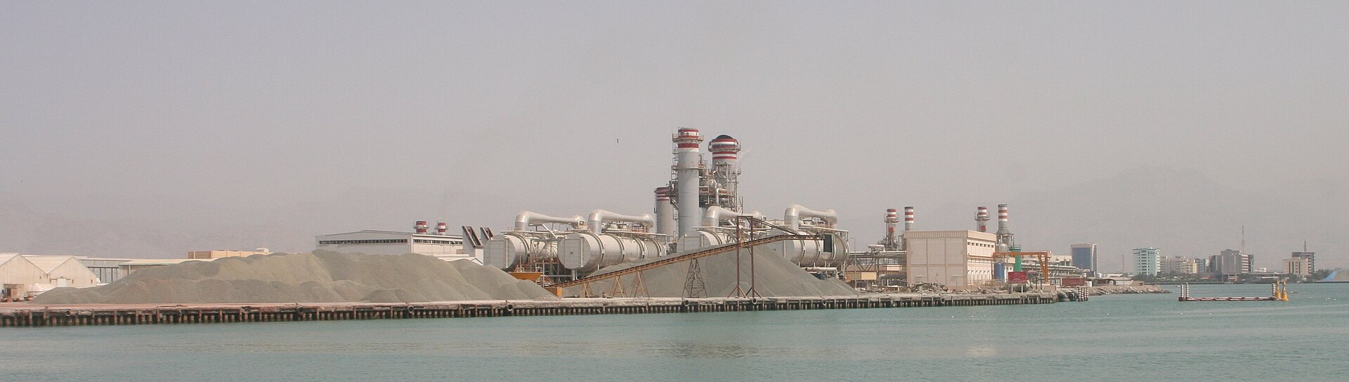 Coastal desalination and power plant in Ras Al Khaimah, UAE, on the Persian Gulf — showing industrial pipes, chimneys, and water intake infrastructure typical of Gulf co-production facilities