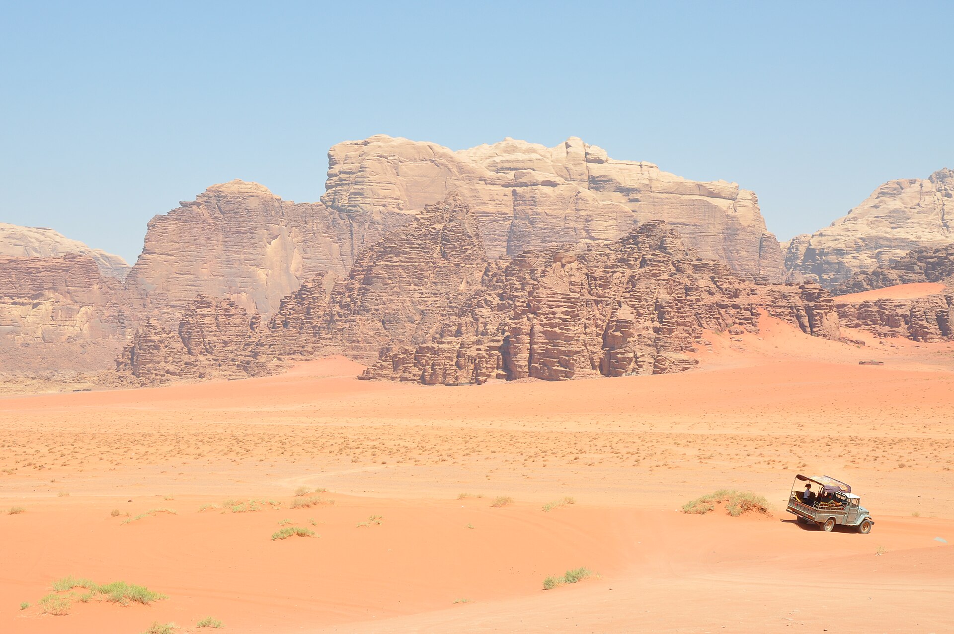 A white 4x4 SUV driving through red desert sand with rocky formations in the background