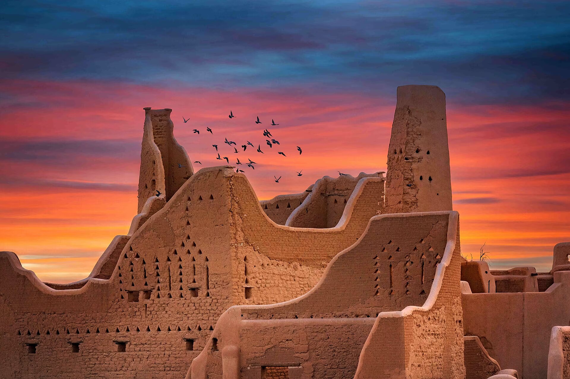Mud-brick Najdi architecture of At-Turaif District in Diriyah at sunset with birds flying overhead