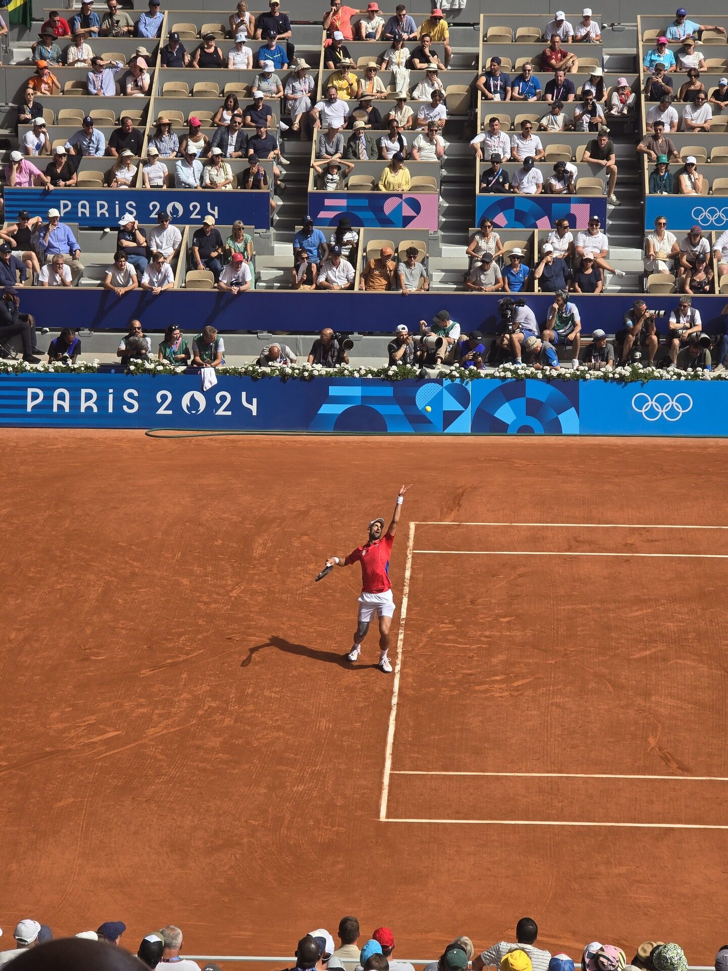 Overhead view of Carlos Alcaraz playing on a clay tennis court at the 2024 Paris Olympics, both Alcaraz and Djokovic have competed at the Six Kings Slam in Riyadh