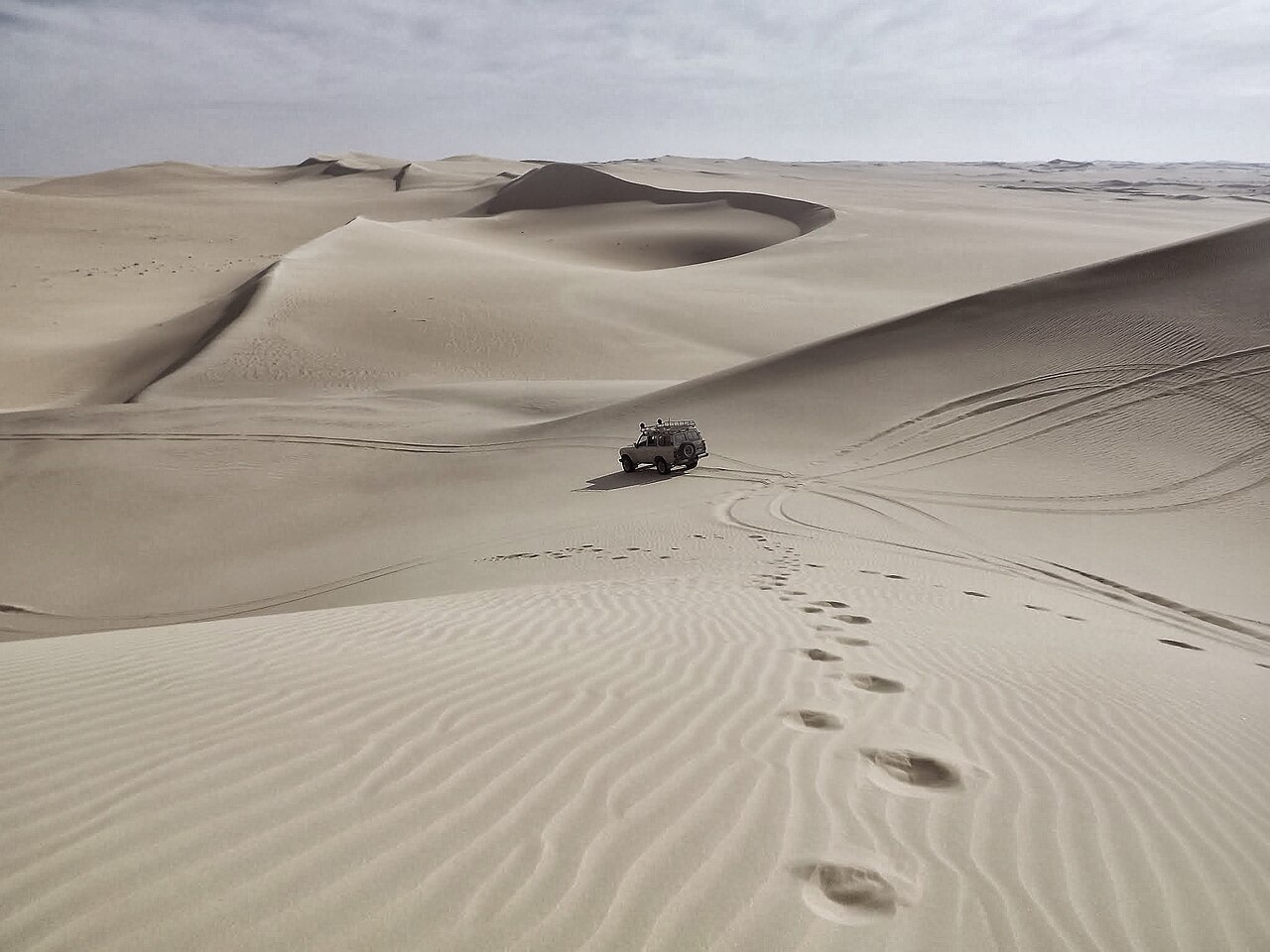 White Toyota Land Cruiser 4WD vehicle navigating vast sand dunes in the Arabian desert