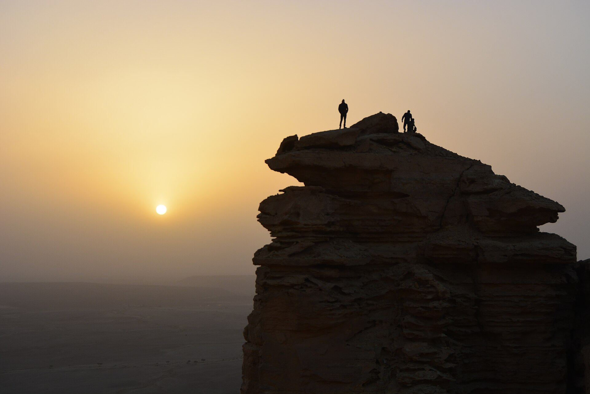 Silhouetted hikers standing on the Edge of the World escarpment near Riyadh at sunset