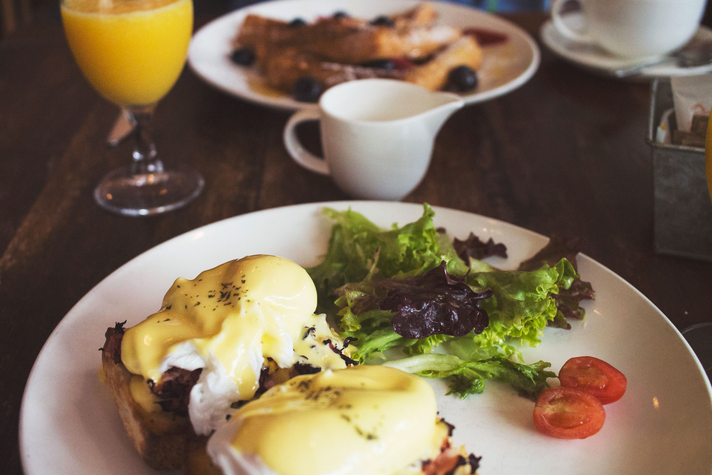 Eggs Benedict with hollandaise sauce served at a brunch restaurant with orange juice and French toast