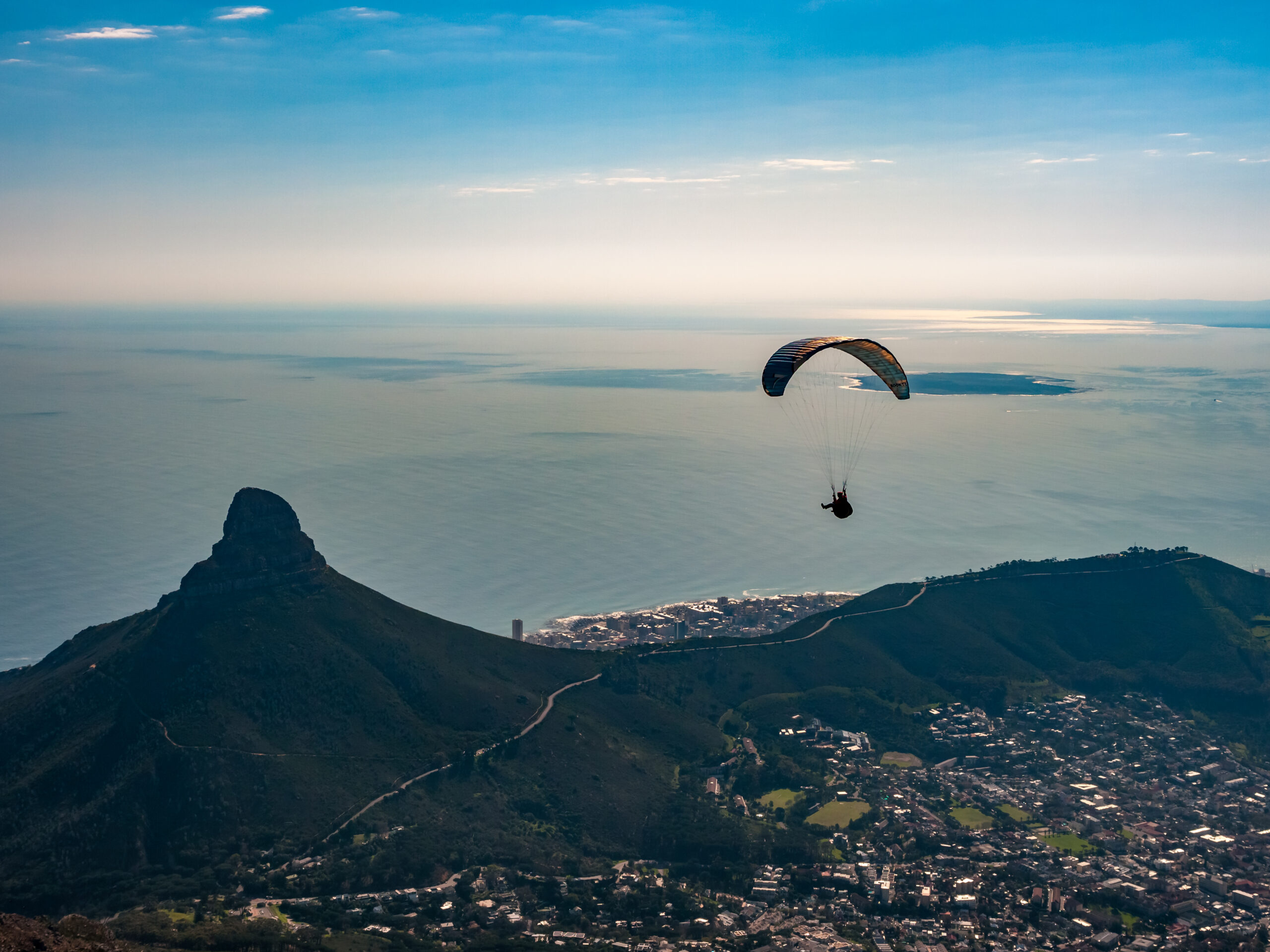 Paraglider soaring above mountain peaks with ocean backdrop