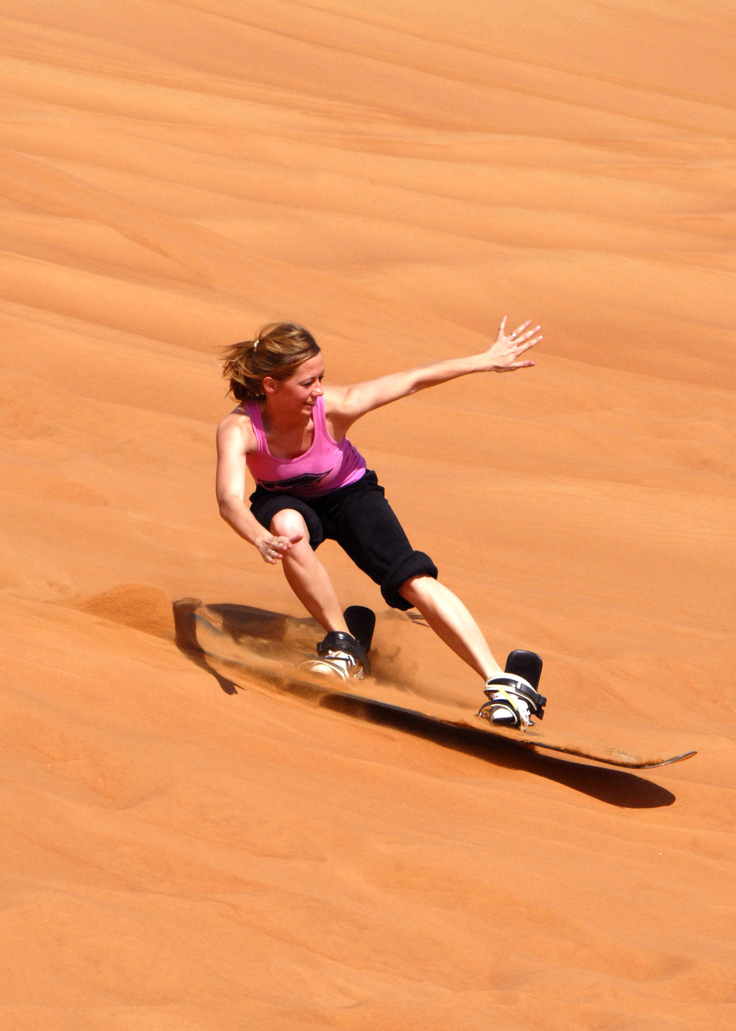 Sandboarder carving down an orange sand dune