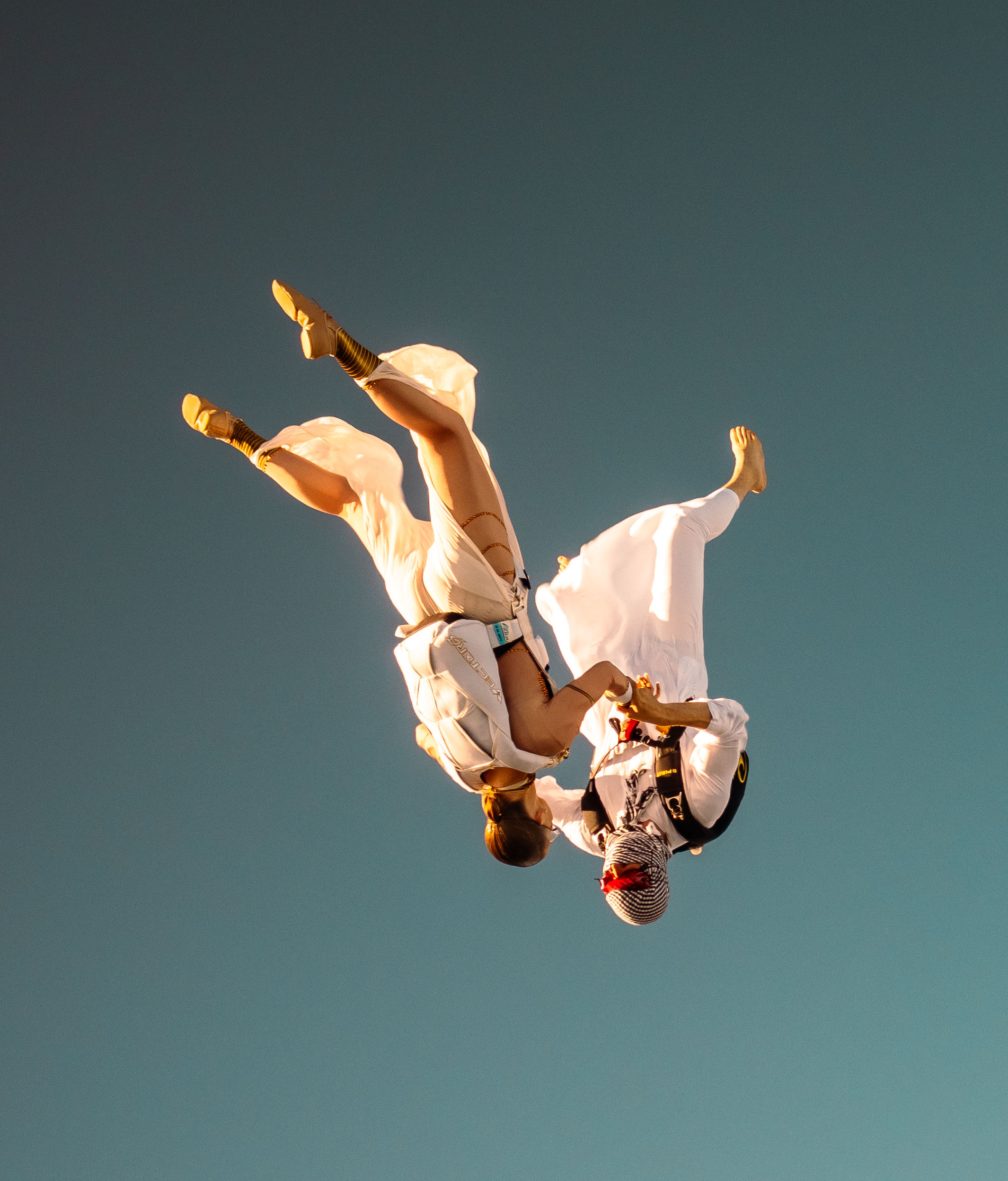 Two skydivers performing acrobatic freefall against a sunset sky