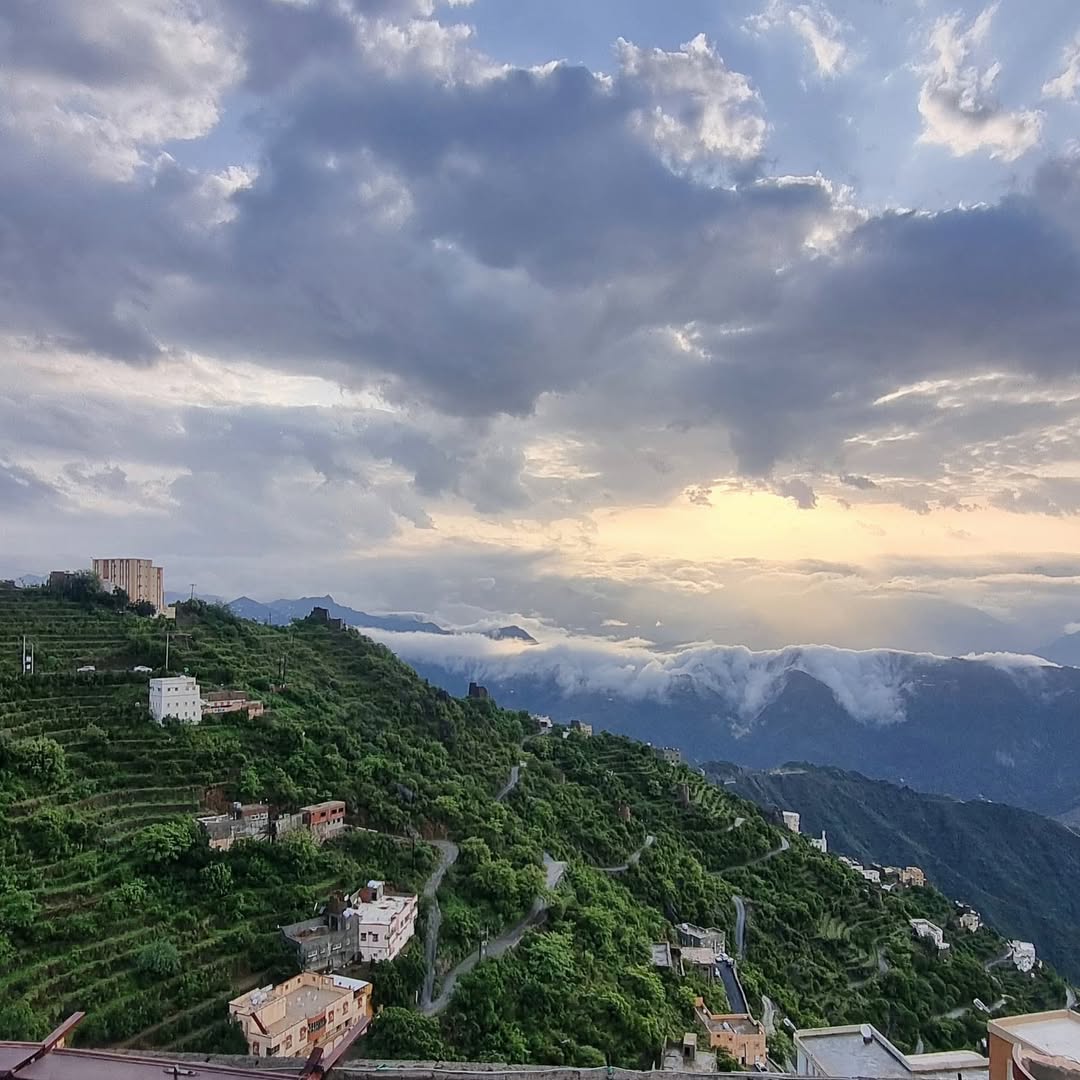 Faifa Mountains in Jizan Province, Saudi Arabia, with terraced green hillsides, winding roads, and dramatic clouds at sunset