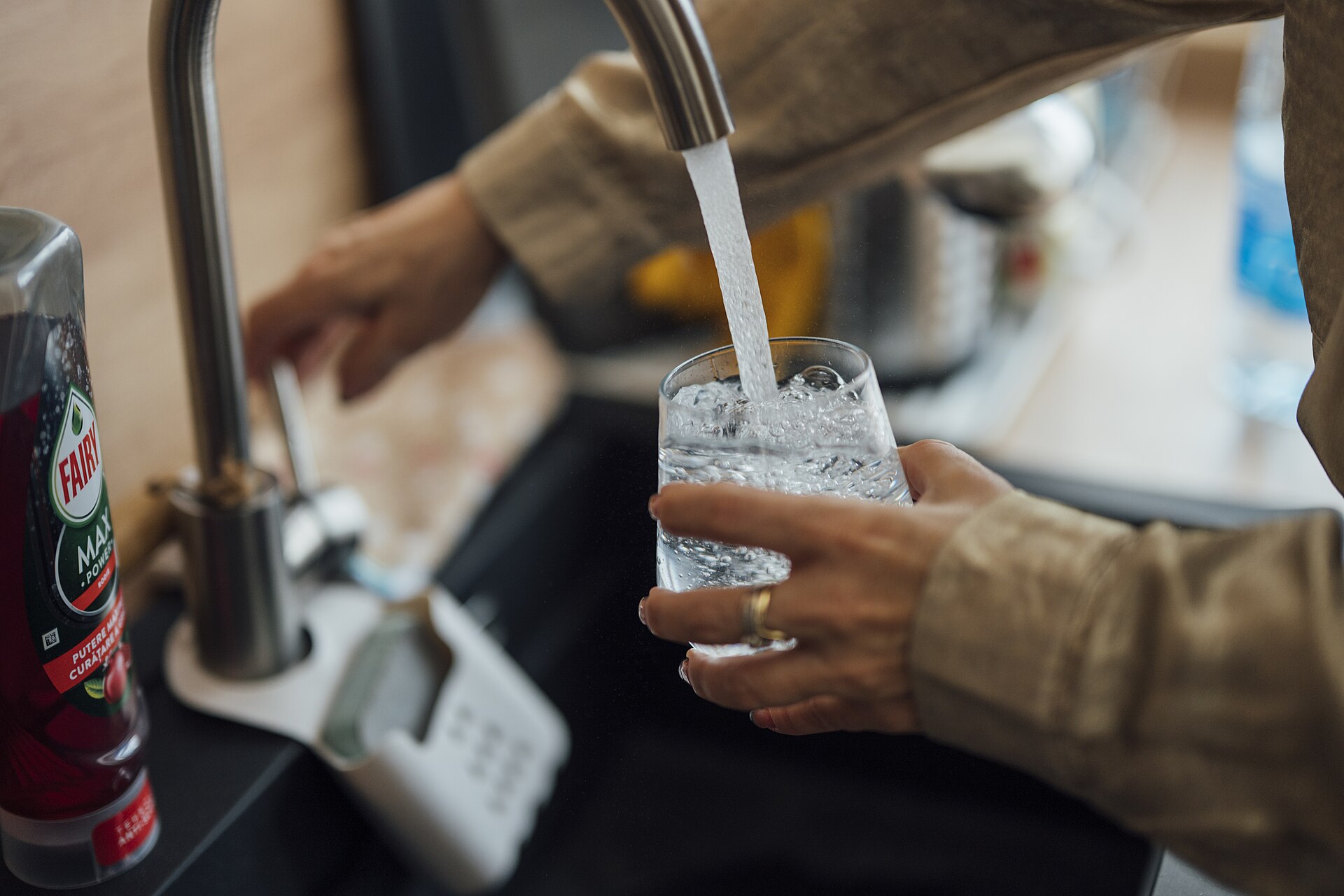 Person filling a clear glass with tap water from a kitchen faucet