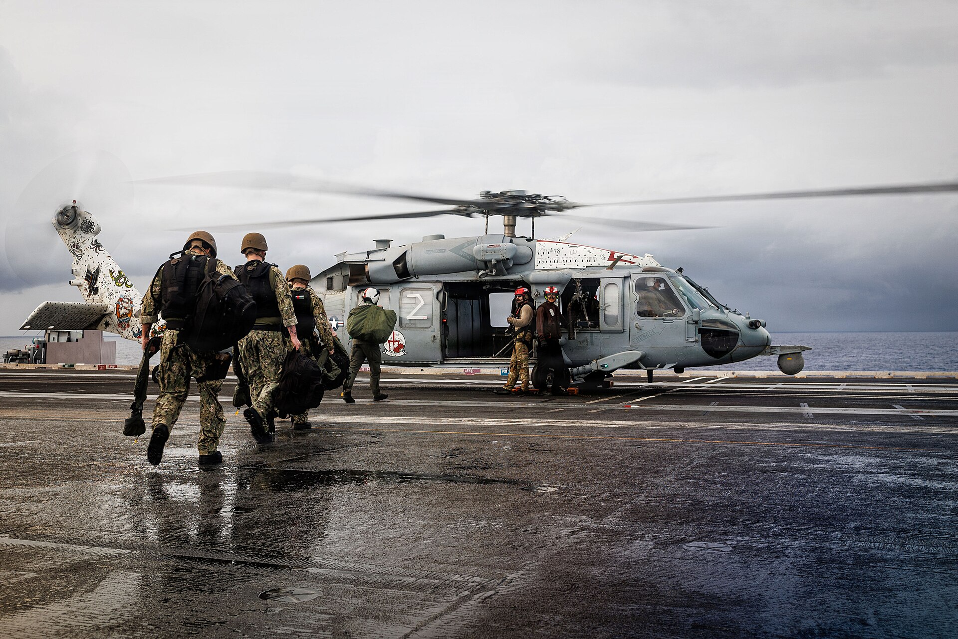 US Navy sailors board an MH-60S Sea Hawk helicopter on USS Gerald R. Ford flight deck ahead of a right-of-visit boarding operation, illustrating the enforcement mechanics of the CENTCOM blockade.