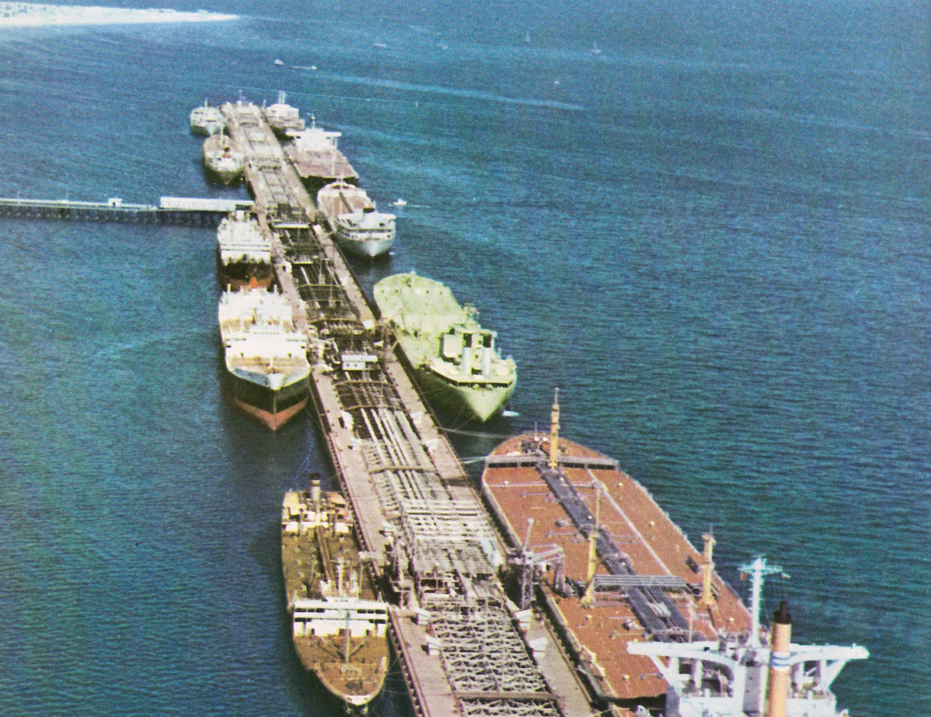 Aerial view of an offshore oil loading terminal in the Persian Gulf with multiple large tankers moored alongside the pipeline pier — the type of infrastructure that underpins Gulf crude export capacity