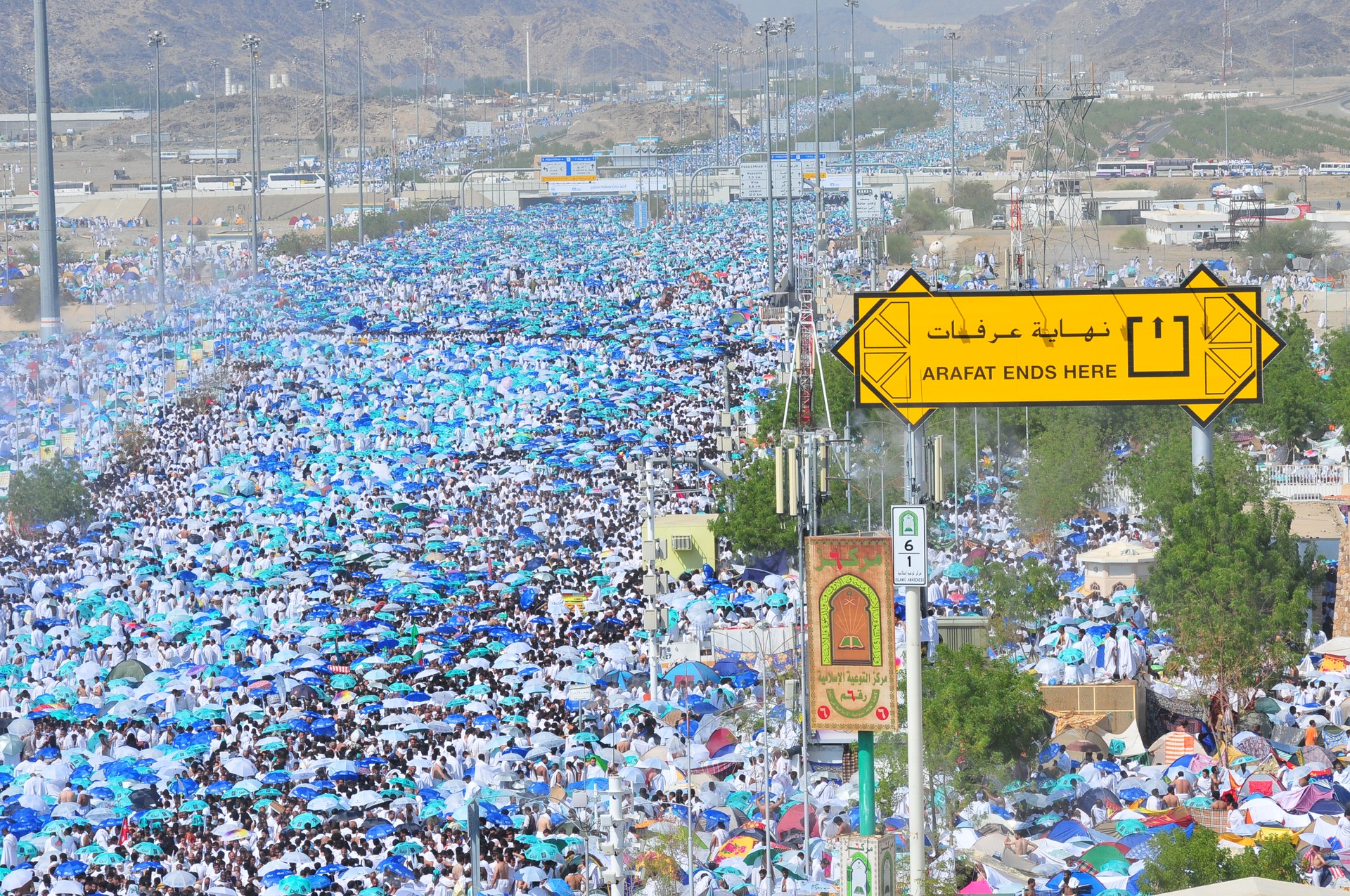 Hundreds of thousands of Hajj pilgrims in white ihram garments crowd the plain of Arafat at the boundary sign marking the sacred boundary of the Arafat site