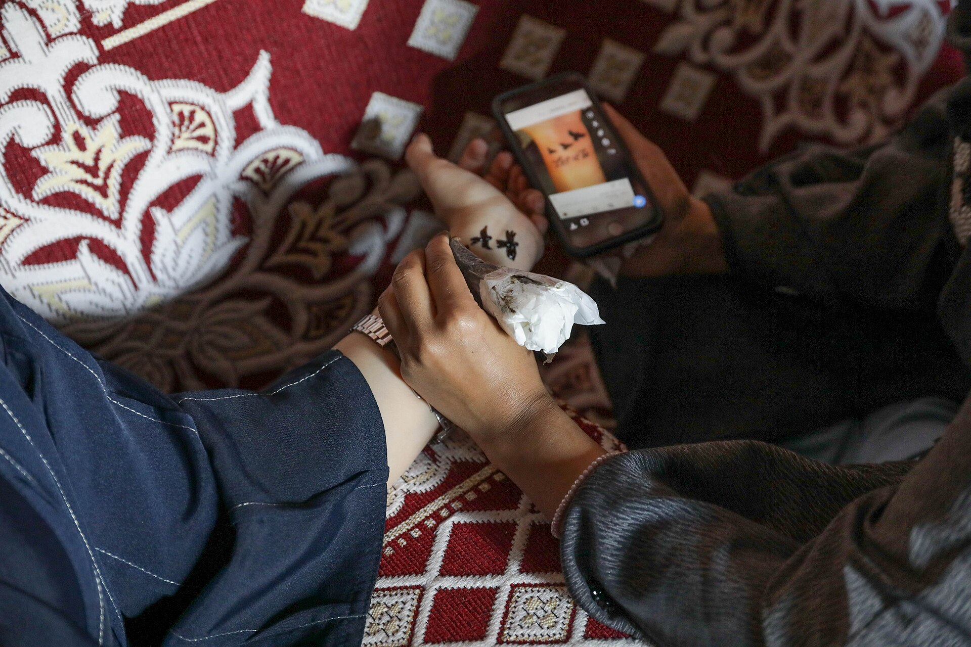A Saudi woman applying traditional henna designs on a hand, seated on traditional textiles