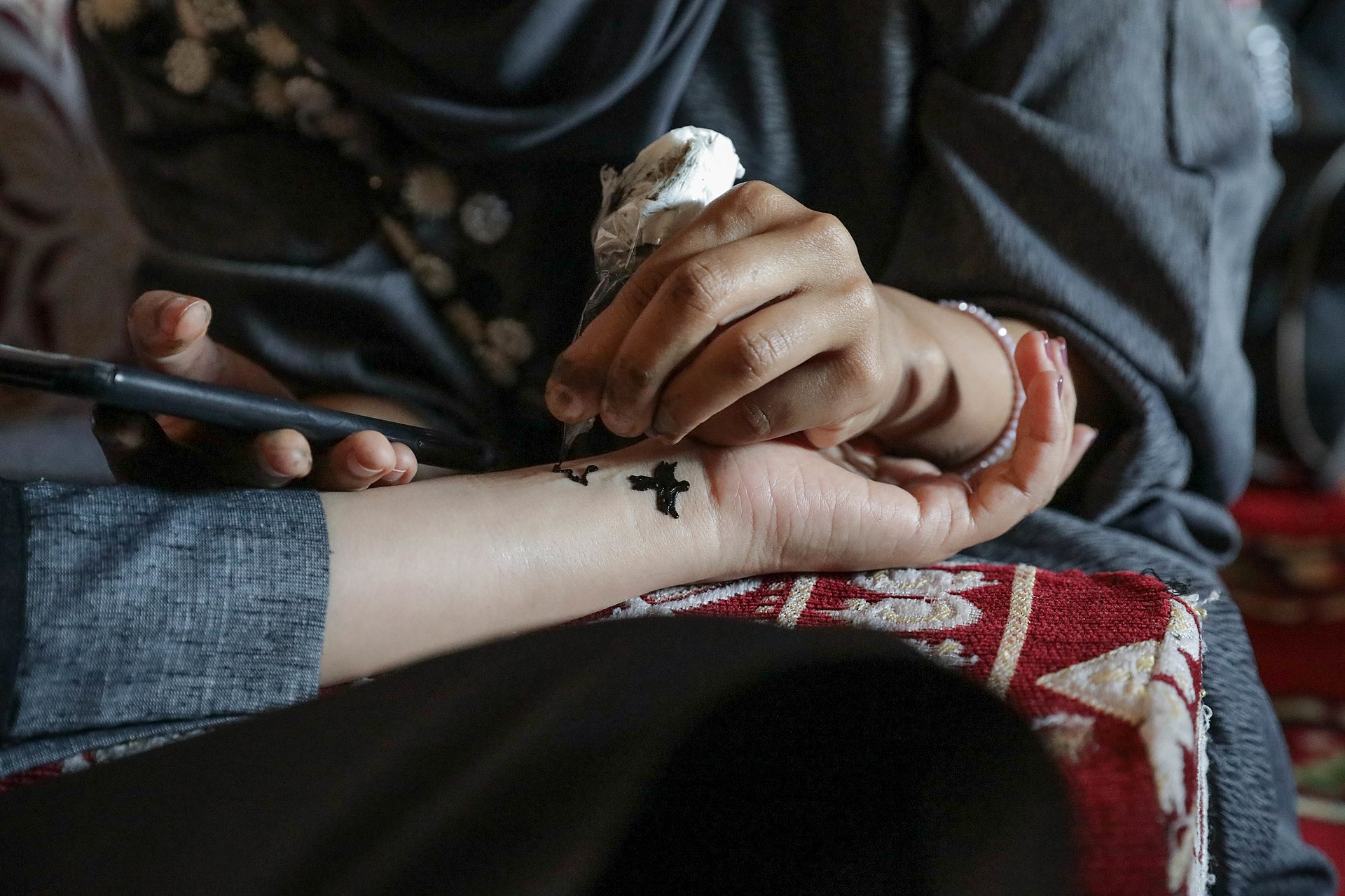 Close-up of a Saudi woman applying henna designs to a hand using a traditional cone