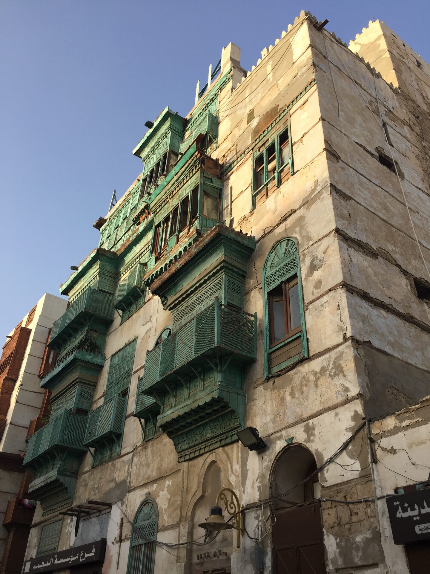 Traditional coral-stone tower house with green wooden mashrabiya balconies in Al-Balad, historic Jeddah