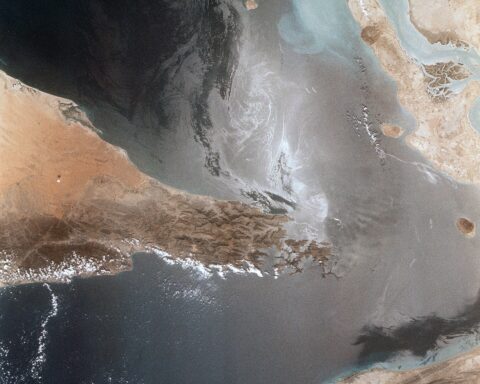 Space Shuttle orbital photograph of the Strait of Hormuz showing the narrow shipping channel between Iran and Oman with oil slick patterns and sunglint visible in the Persian Gulf