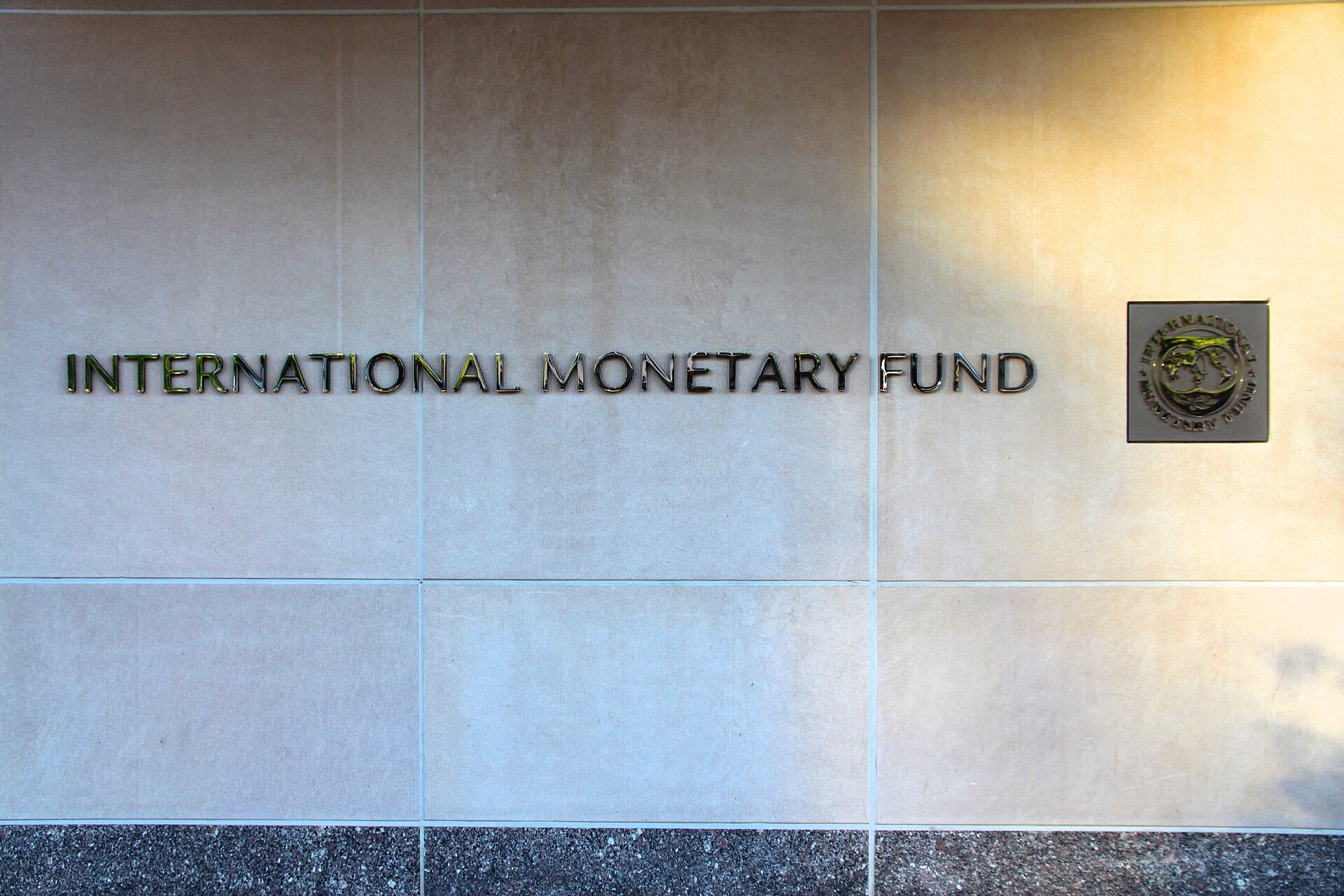 International Monetary Fund sign on IMF headquarters facade in Washington DC — the institution whose April 2026 WEO used commodity price data from February-March, missing the US naval blockade of Iranian ports enacted April 13