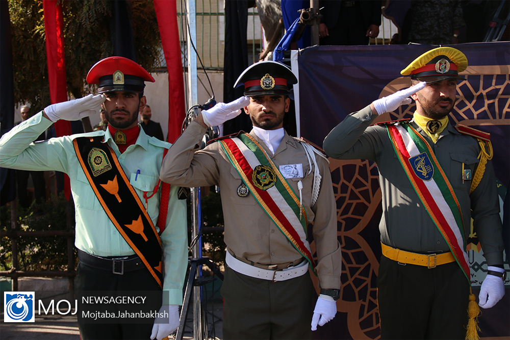 Iranian military officers in ceremonial dress salute during 2019 Sacred Defence Week parade, IRGC insignia visible on right figure