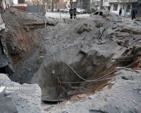 A bomb crater in a residential street in Tehran following coalition airstrikes, with emergency workers surveying the damage. Photo: Avash Media / CC BY 4.0