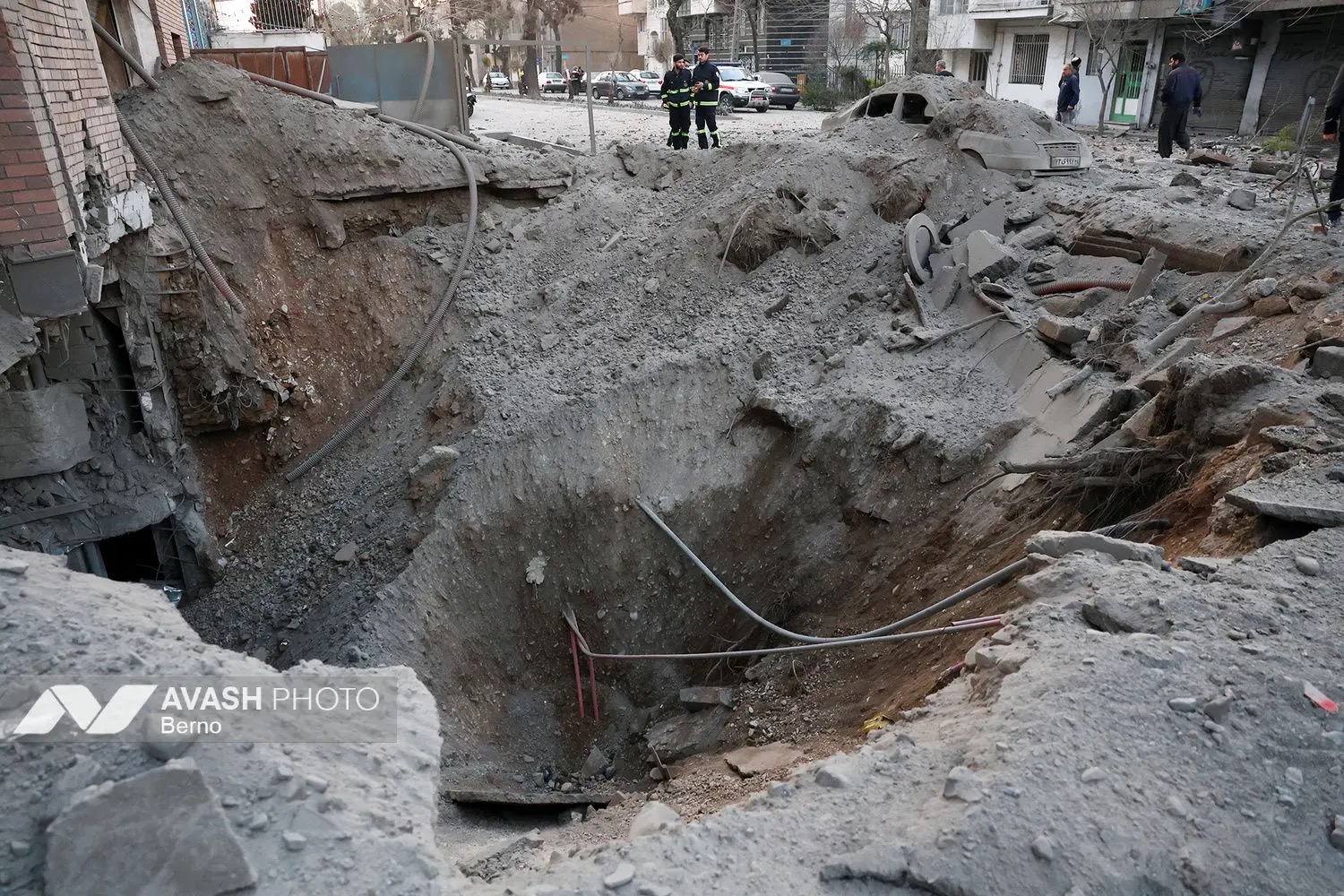 A bomb crater in a residential street in Tehran following coalition airstrikes, with emergency workers surveying the damage. Photo: Avash Media / CC BY 4.0