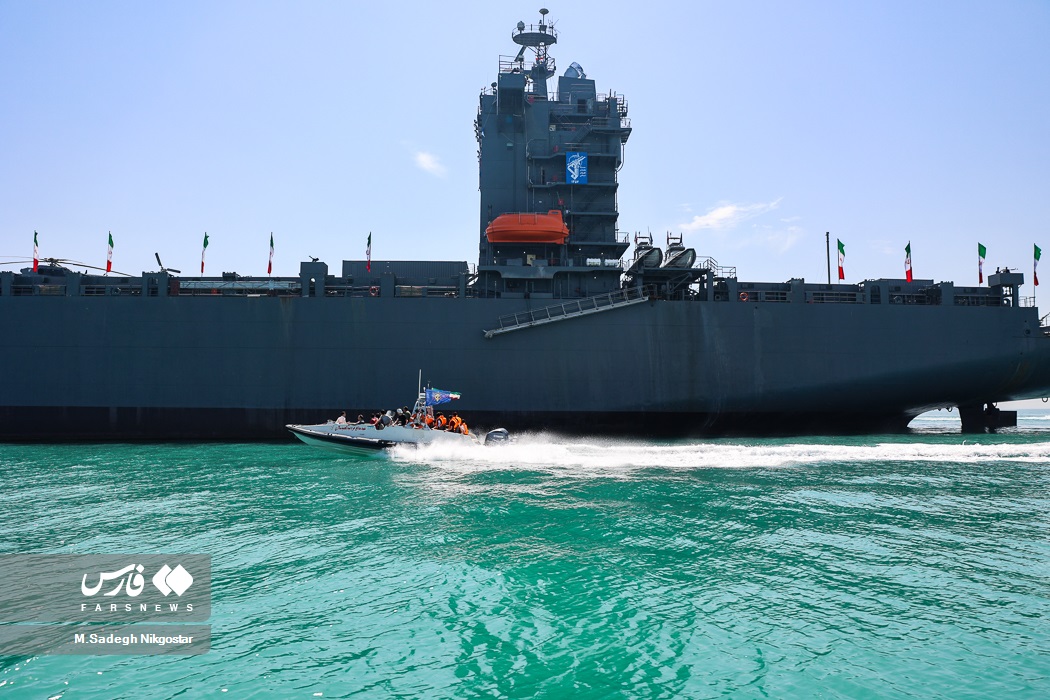 IRGC Navy fast-attack speedboat alongside a large IRGC naval vessel at Bandar Abbas, Hormuzgan Province, Iran — the type of small fast craft used to escort and intercept commercial shipping in the Strait of Hormuz