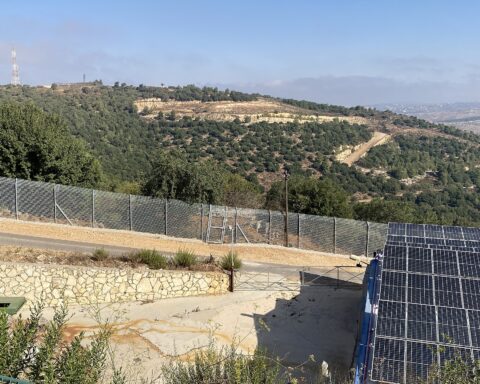 The Israel-Lebanon security fence running through the Galilee hills at the northern Israeli border, with Lebanese territory visible beyond the barrier