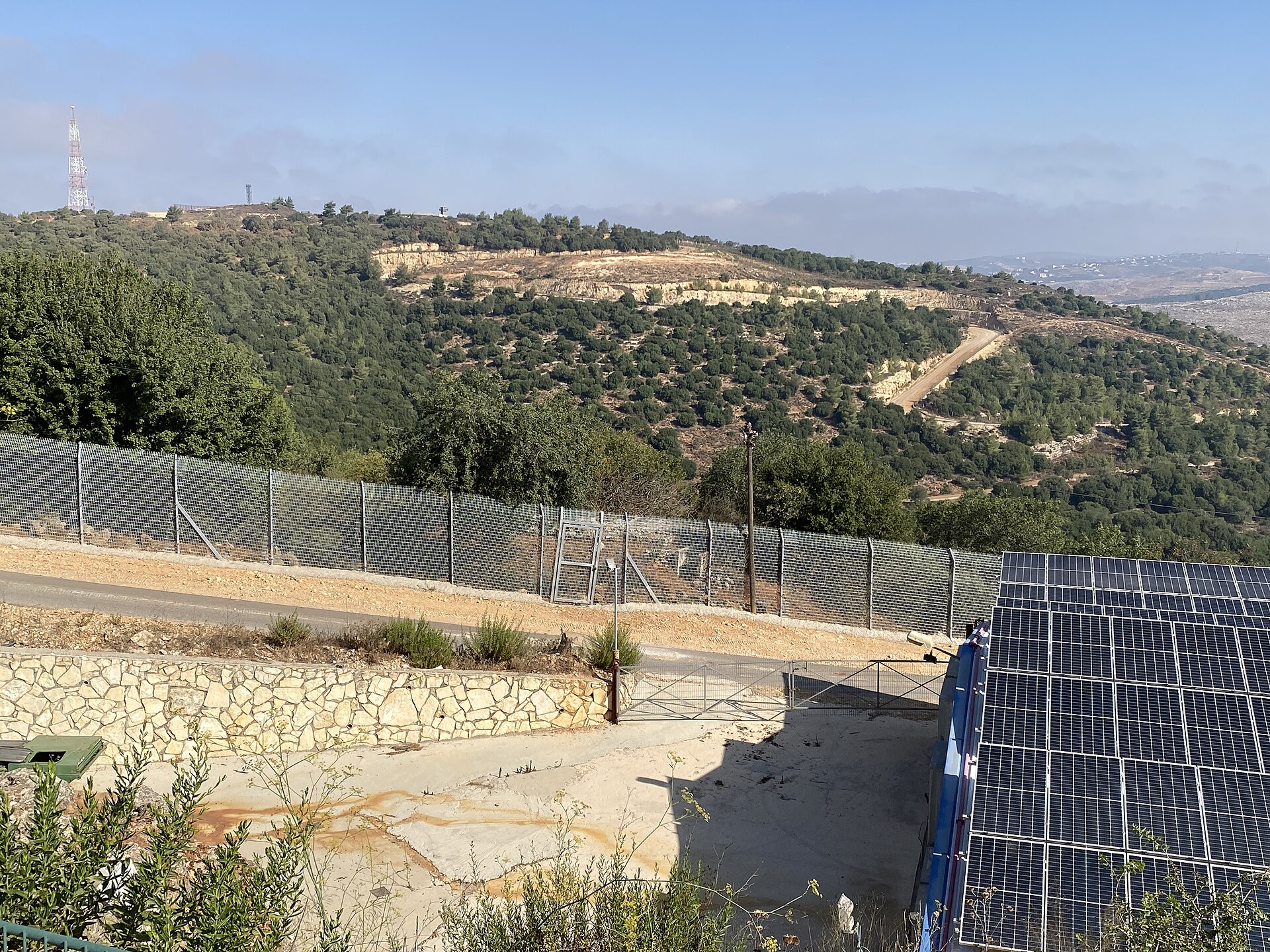 The Israel-Lebanon security fence running through the Galilee hills at the northern Israeli border, with Lebanese territory visible beyond the barrier