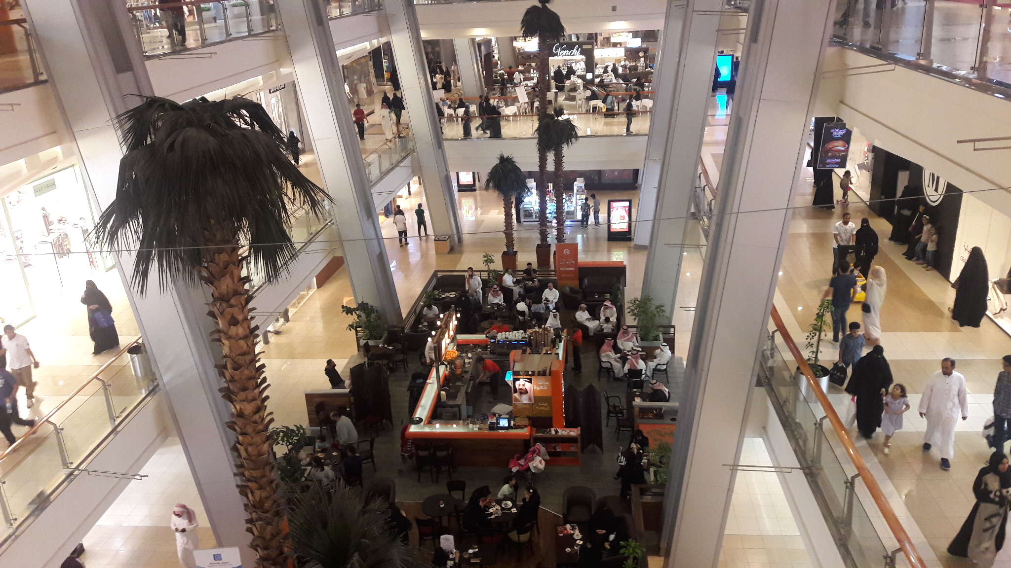 Interior atrium of Red Sea Mall in Jeddah showing multiple shopping levels, palm trees, and shoppers