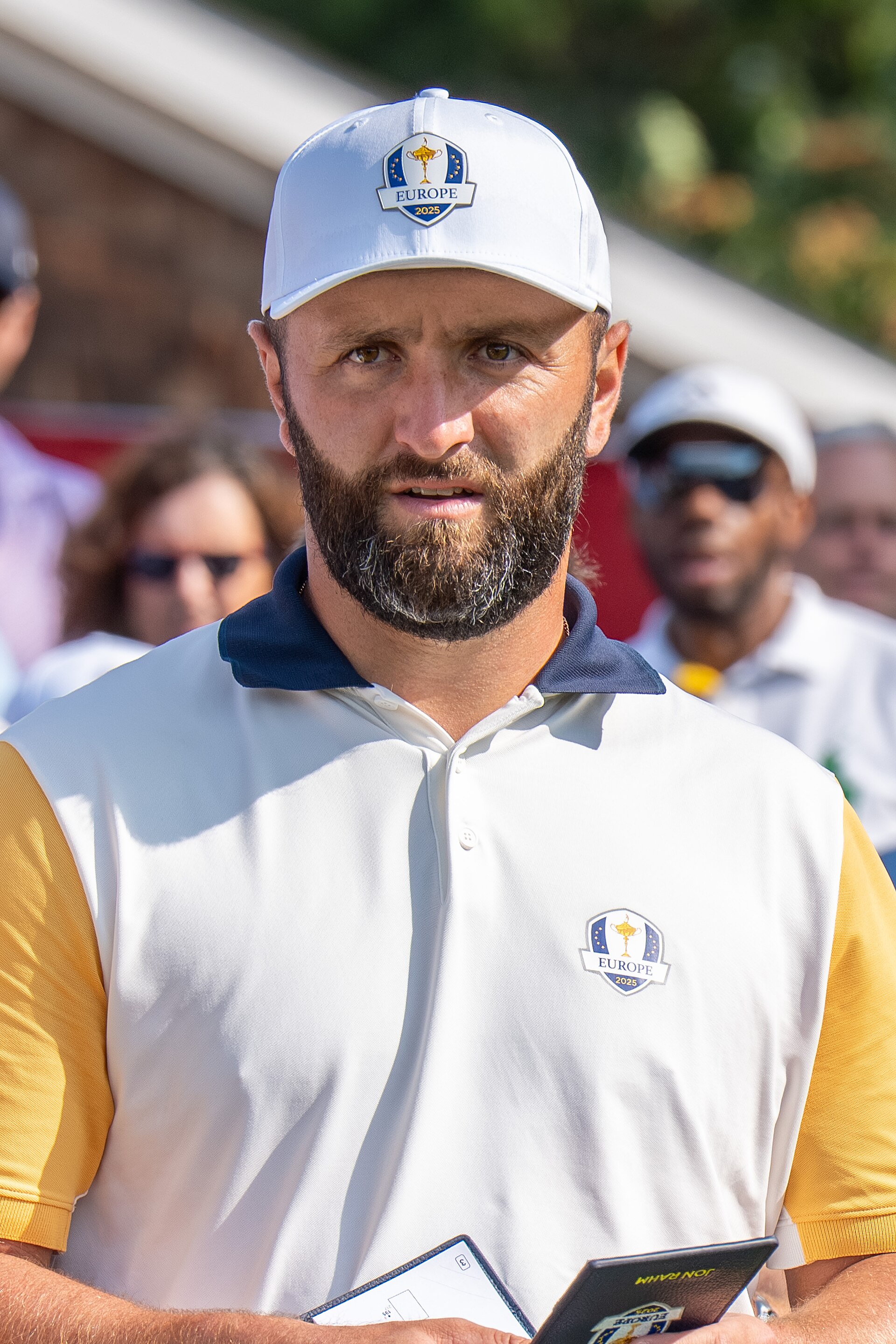 Jon Rahm at a professional golf event wearing a white polo and cap