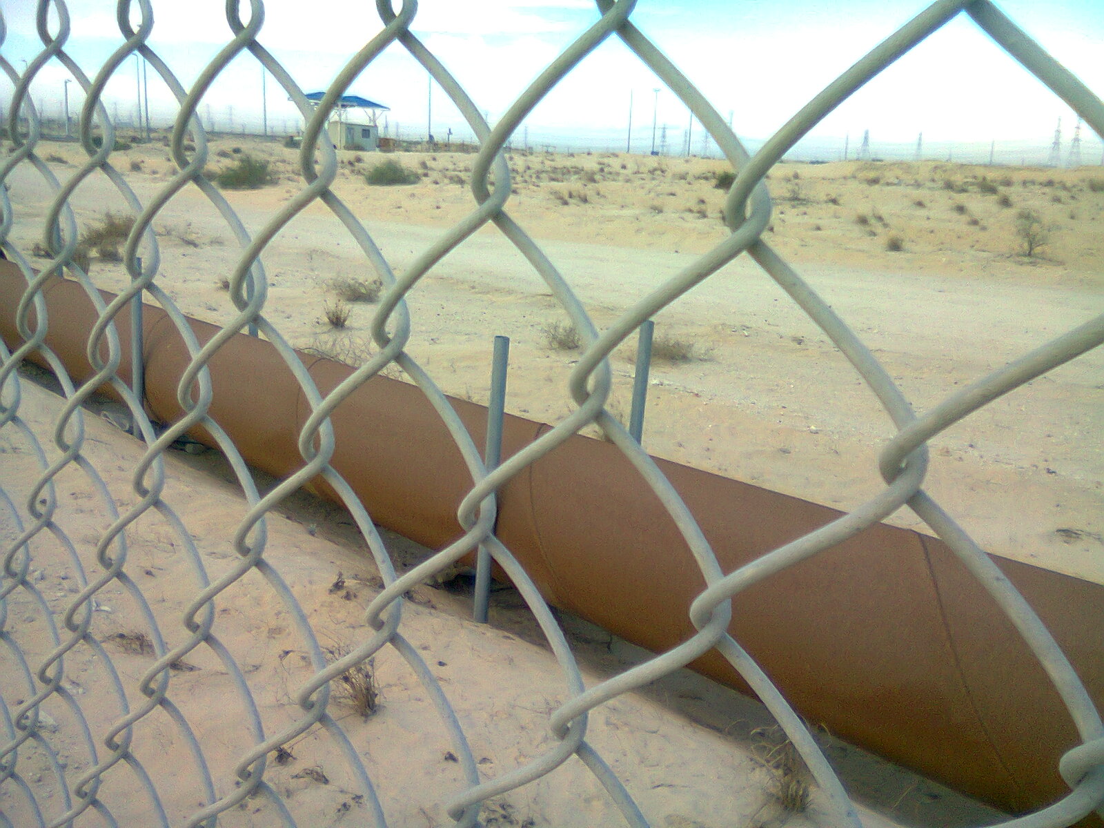 Oil pipeline crossing the Jubail desert in Saudi Arabia, secured behind chain-link fence
