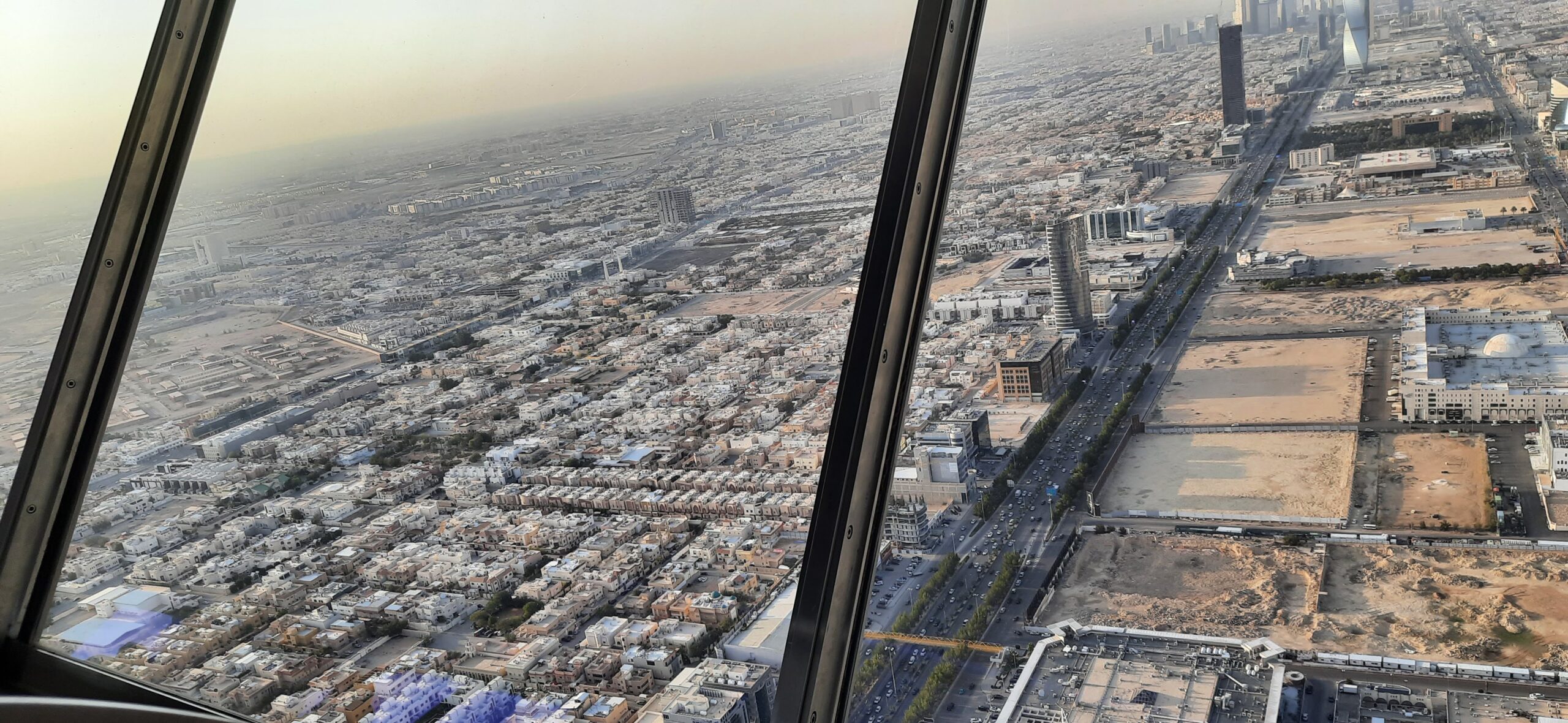 View through the glass panels of the Kingdom Centre Sky Bridge looking out over Riyadh neighbourhoods, with the steel frame of the bridge visible at the edges