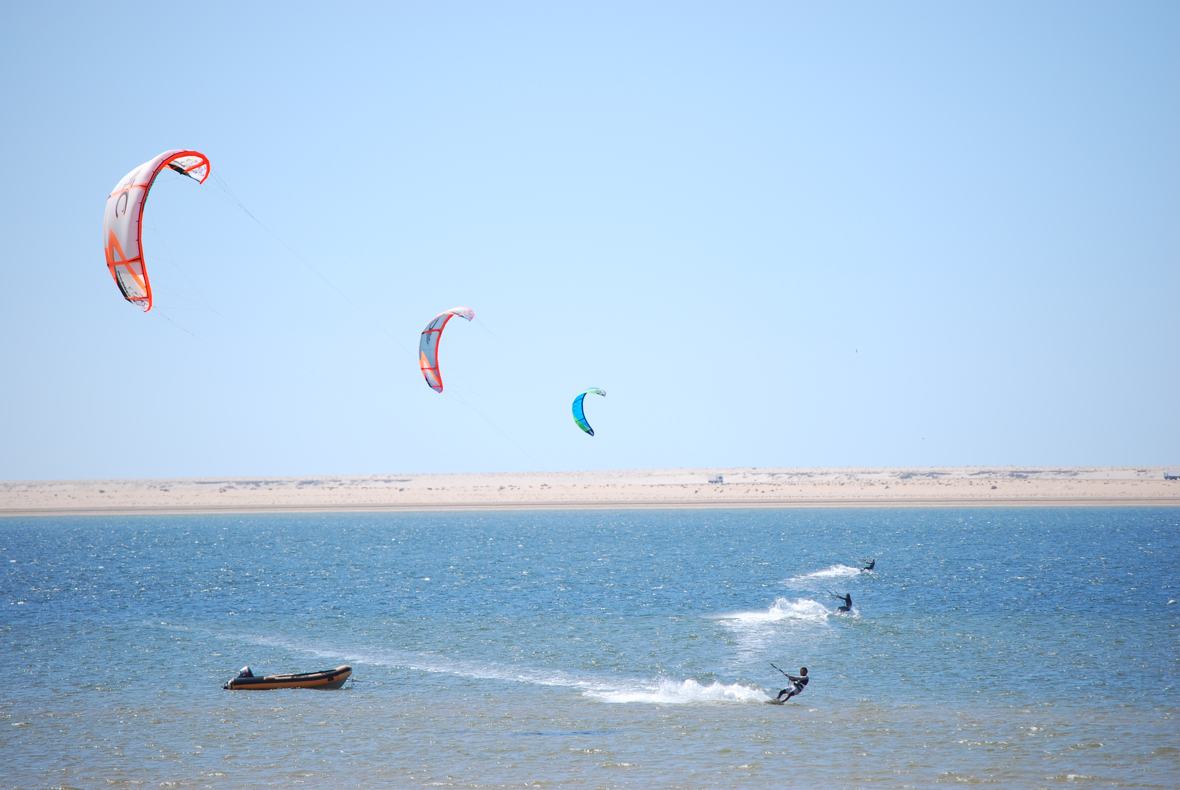 Multiple colourful kites in the sky above a coastal kite surfing session