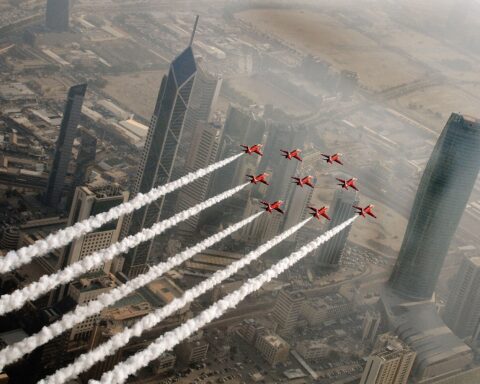 Red Arrows fly in formation over Kuwait City skyline, Al Hamra Tower visible, aerial view of Kuwaiti capital