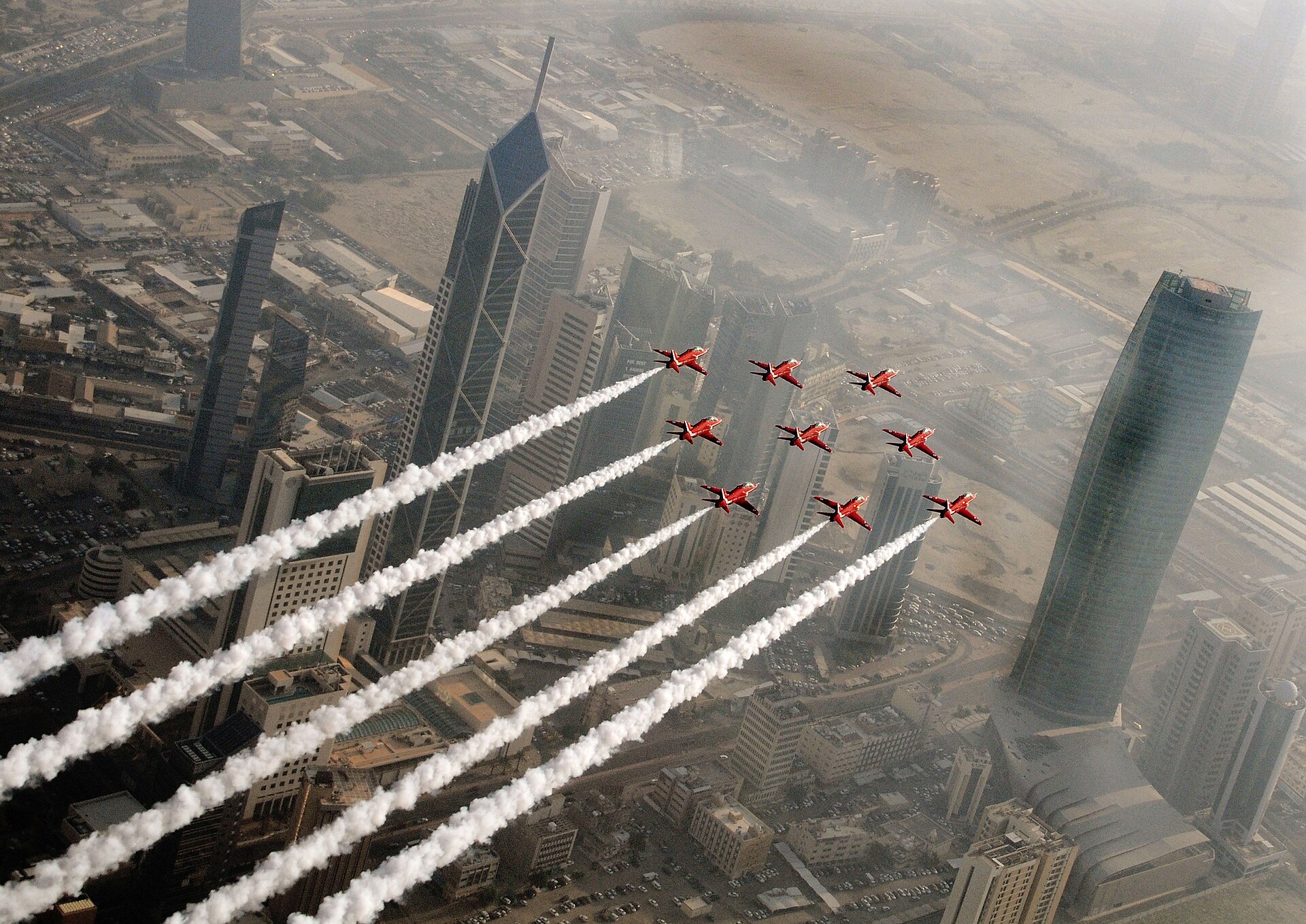 Red Arrows fly in formation over Kuwait City skyline, Al Hamra Tower visible, aerial view of Kuwaiti capital