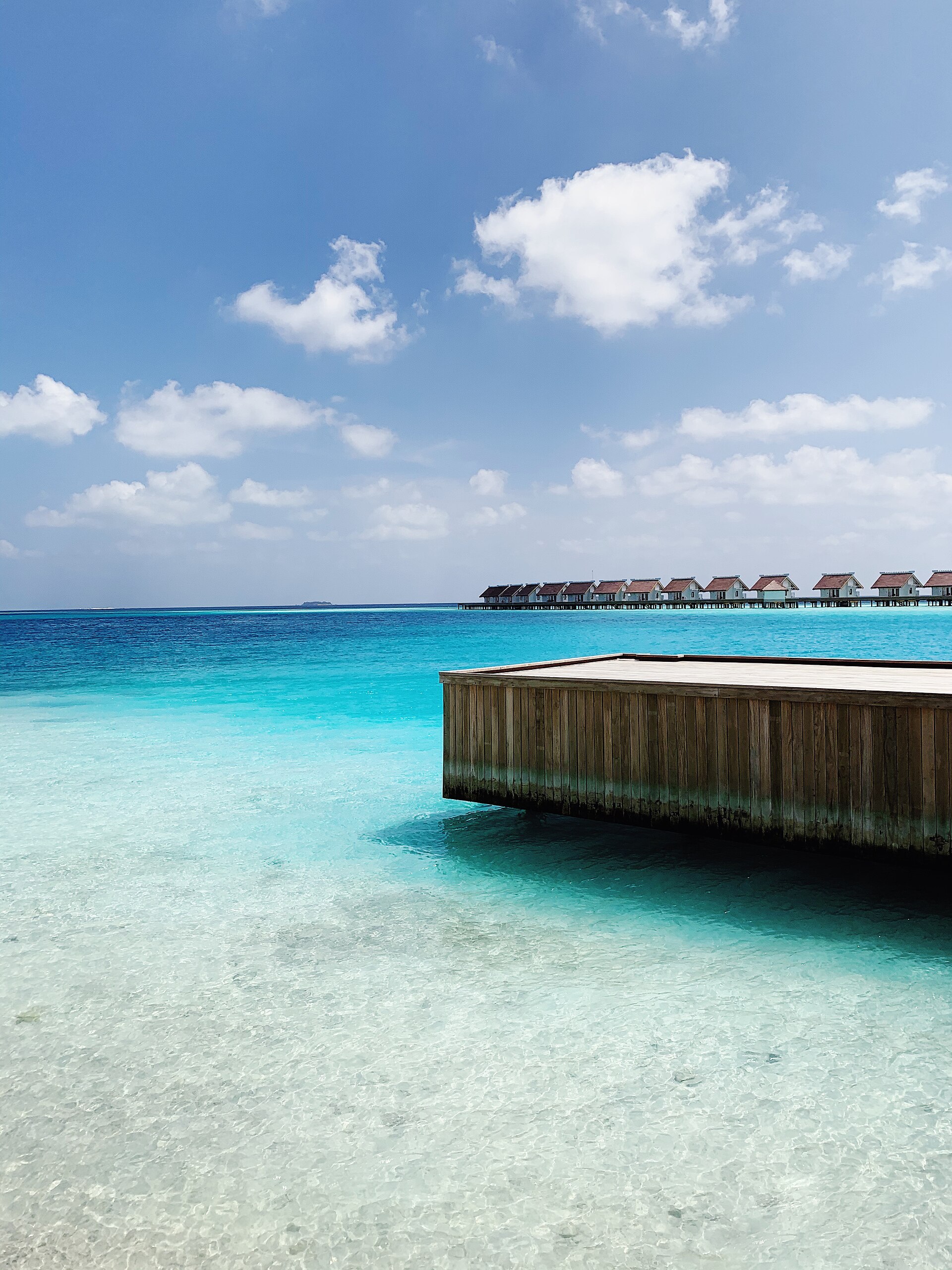 Turquoise lagoon with crystal-clear water and a row of overwater bungalows along the horizon in the Maldives