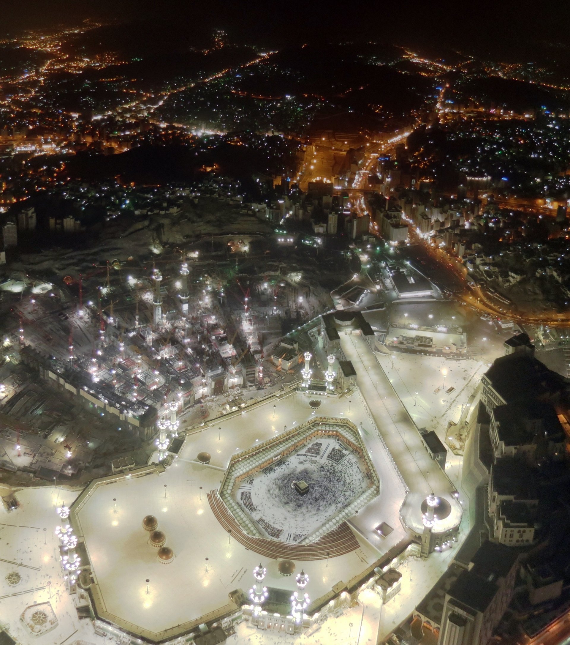 Night aerial view of Masjid al-Haram in Mecca showing the Kaaba surrounded by worshippers and the Grand Mosque complex illuminated