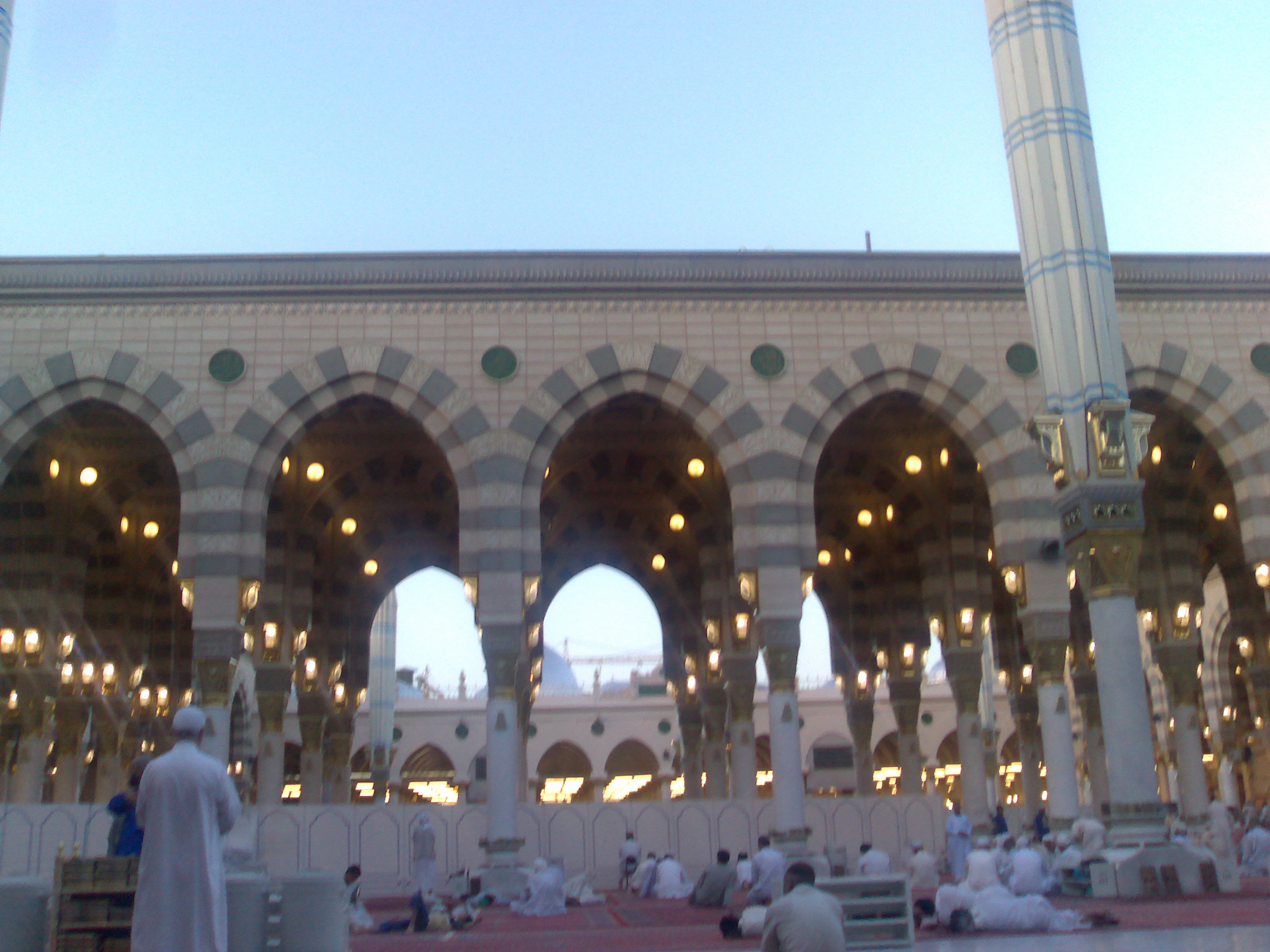 Interior colonnade of Masjid al-Nabawi with ornate arches and worshippers
