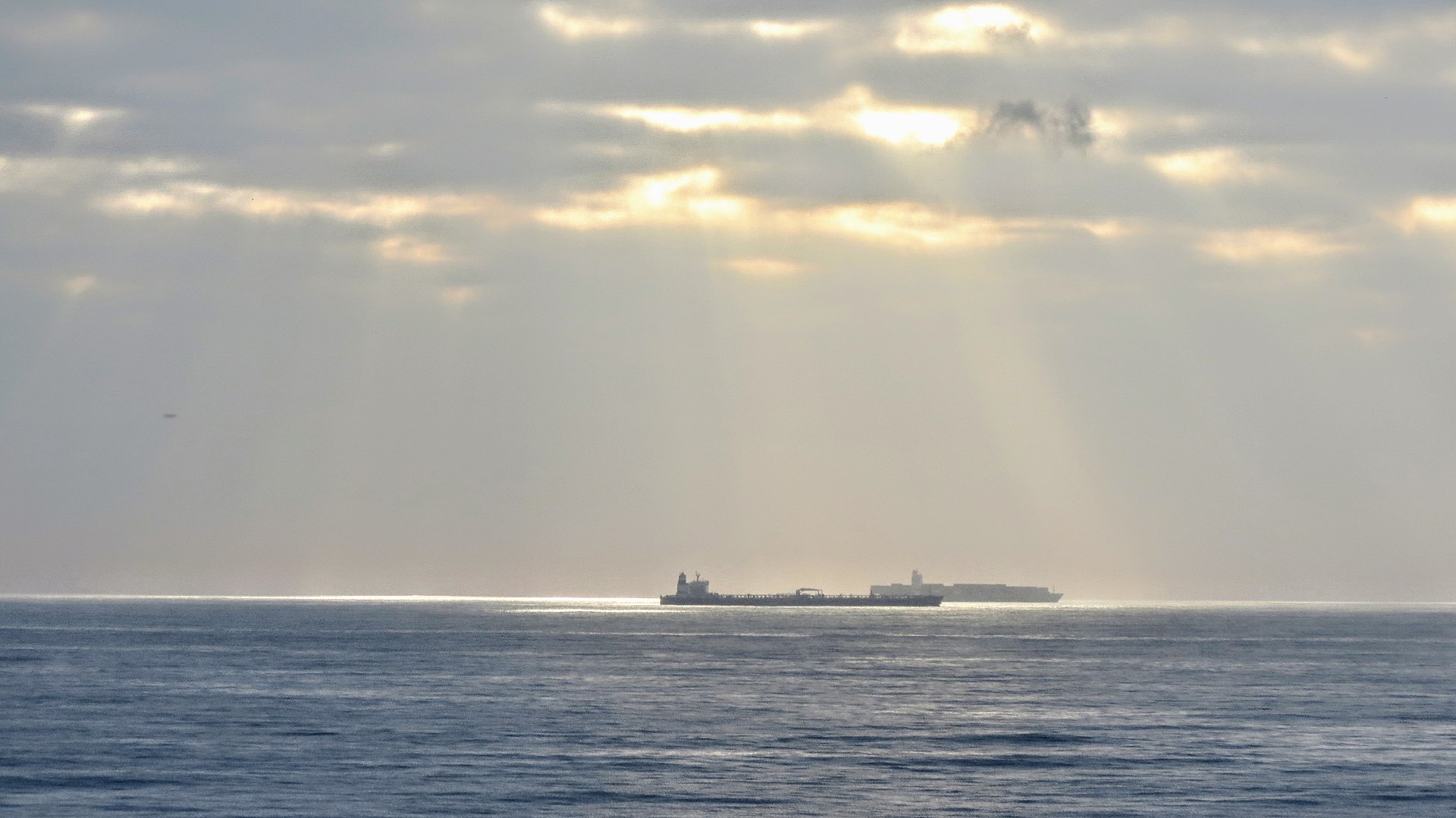 Oil tanker waiting at anchorage, silhouetted against a cloudy sky — the commercial calculus of delay versus risk