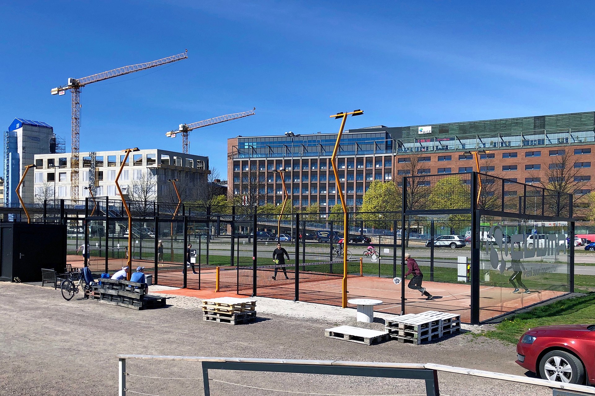 Players on a padel tennis court enclosed by glass walls and metal fencing