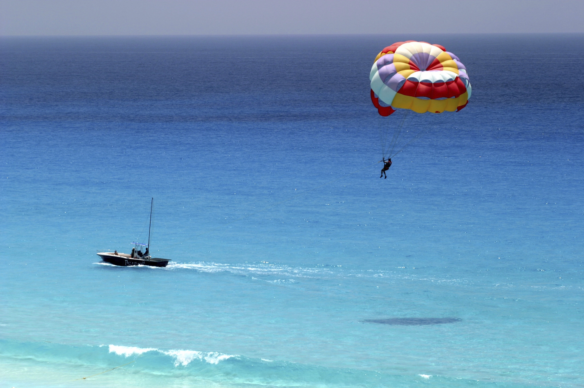 A person parasailing over crystal-clear turquoise water, towed by a speedboat