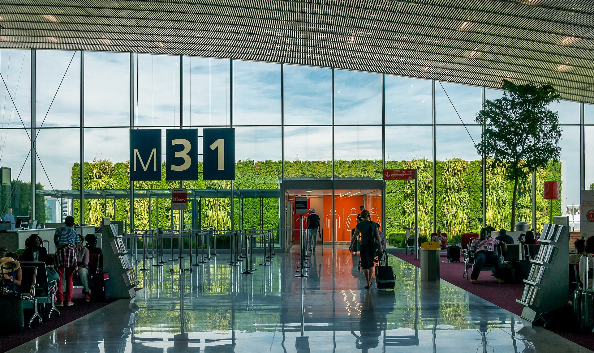 Interior of Paris Charles de Gaulle Airport terminal with glass walls and greenery, gate M31