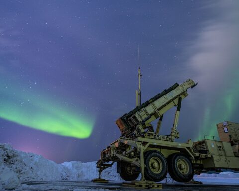 US Air Force Patriot missile air defense battery illuminated by northern lights aurora, missile canisters raised in launch-ready position