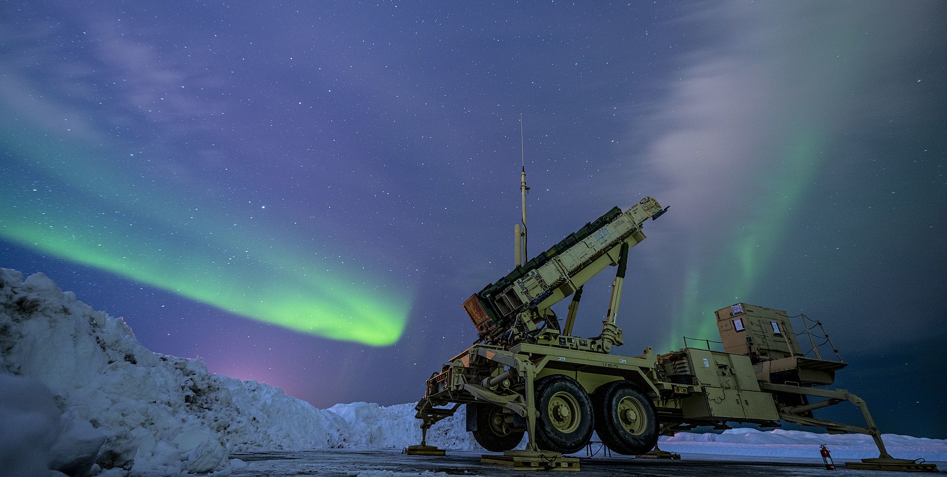 US Air Force Patriot missile air defense battery illuminated by northern lights aurora, missile canisters raised in launch-ready position