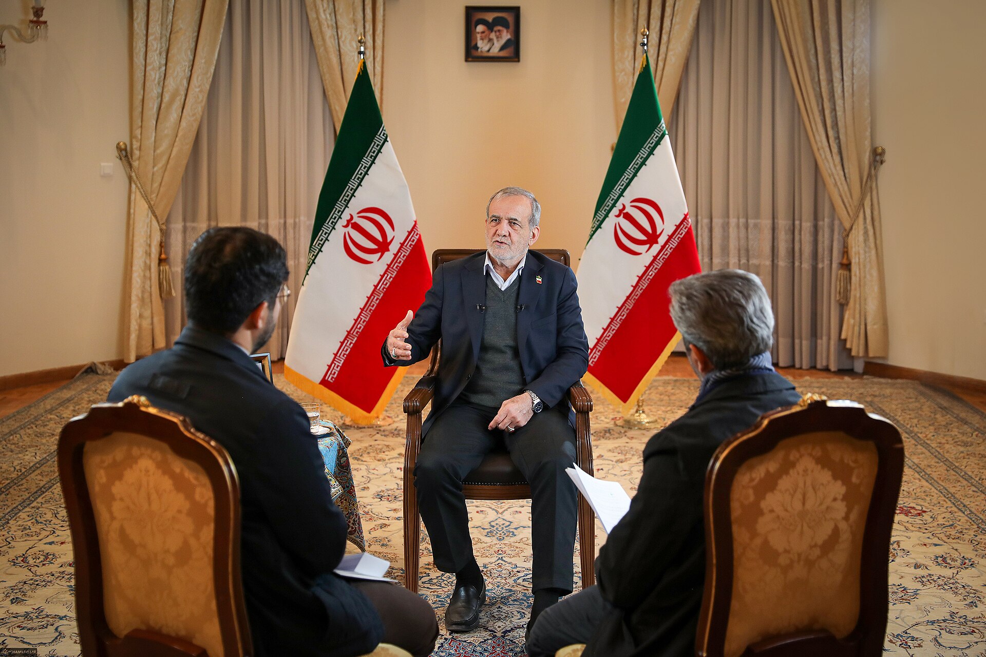 President Pezeshkian speaking in interview, flanked by Iranian flags, 2025