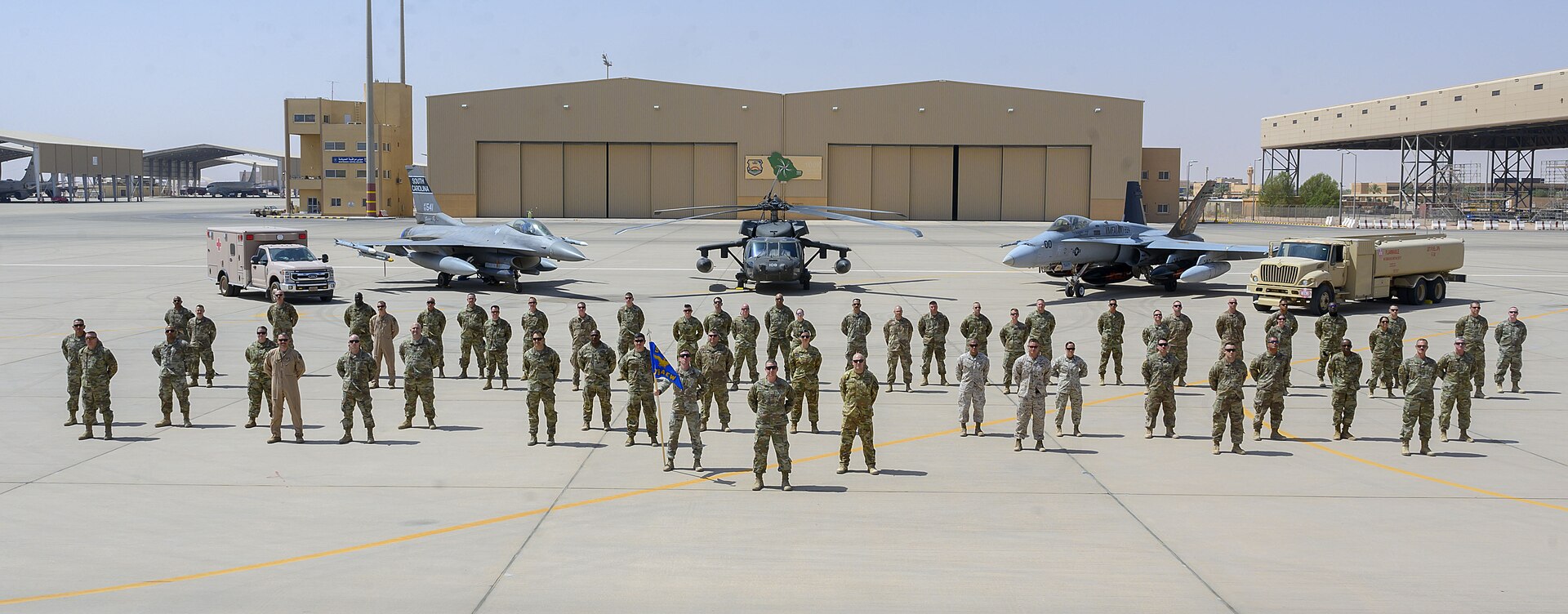 US Air Force personnel and aircraft at Prince Sultan Air Base, Saudi Arabia — F-16s and a helicopter on the apron beneath the Saudi flag